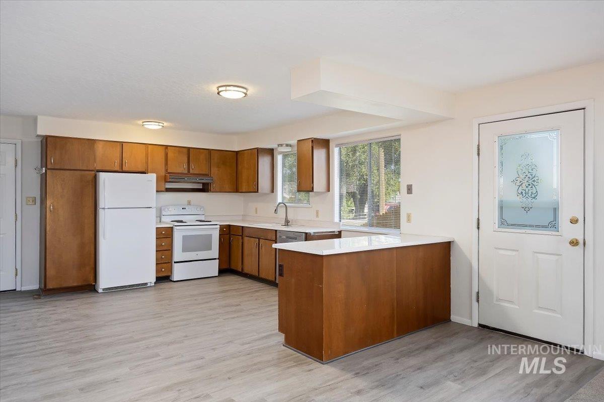 Kitchen with brown cabinets, white appliances, a peninsula, and light wood-style floors