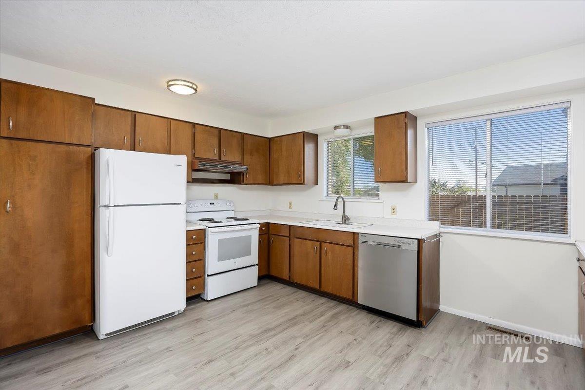 Kitchen featuring white appliances, light countertops, light wood finished floors, brown cabinetry, and under cabinet range hood