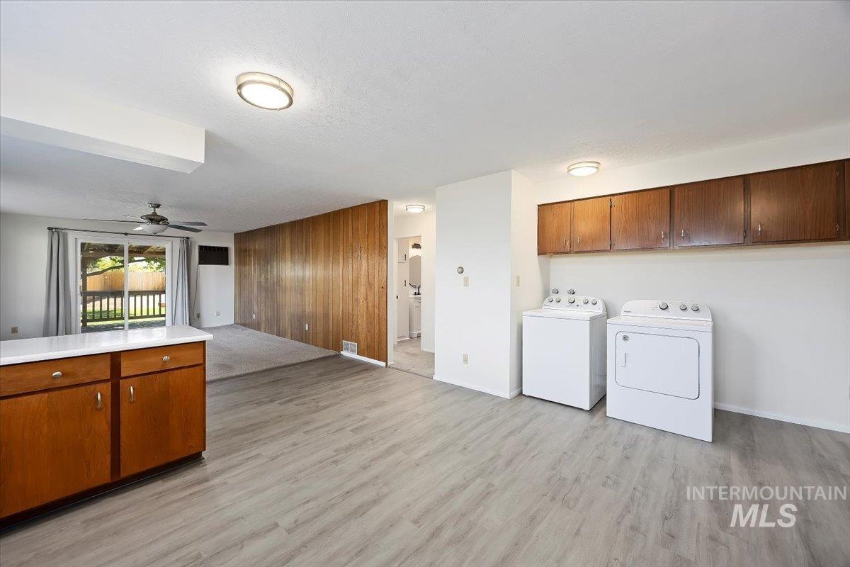 Laundry room featuring cabinet space, wooden walls, separate washer and dryer, a ceiling fan, and light wood finished floors