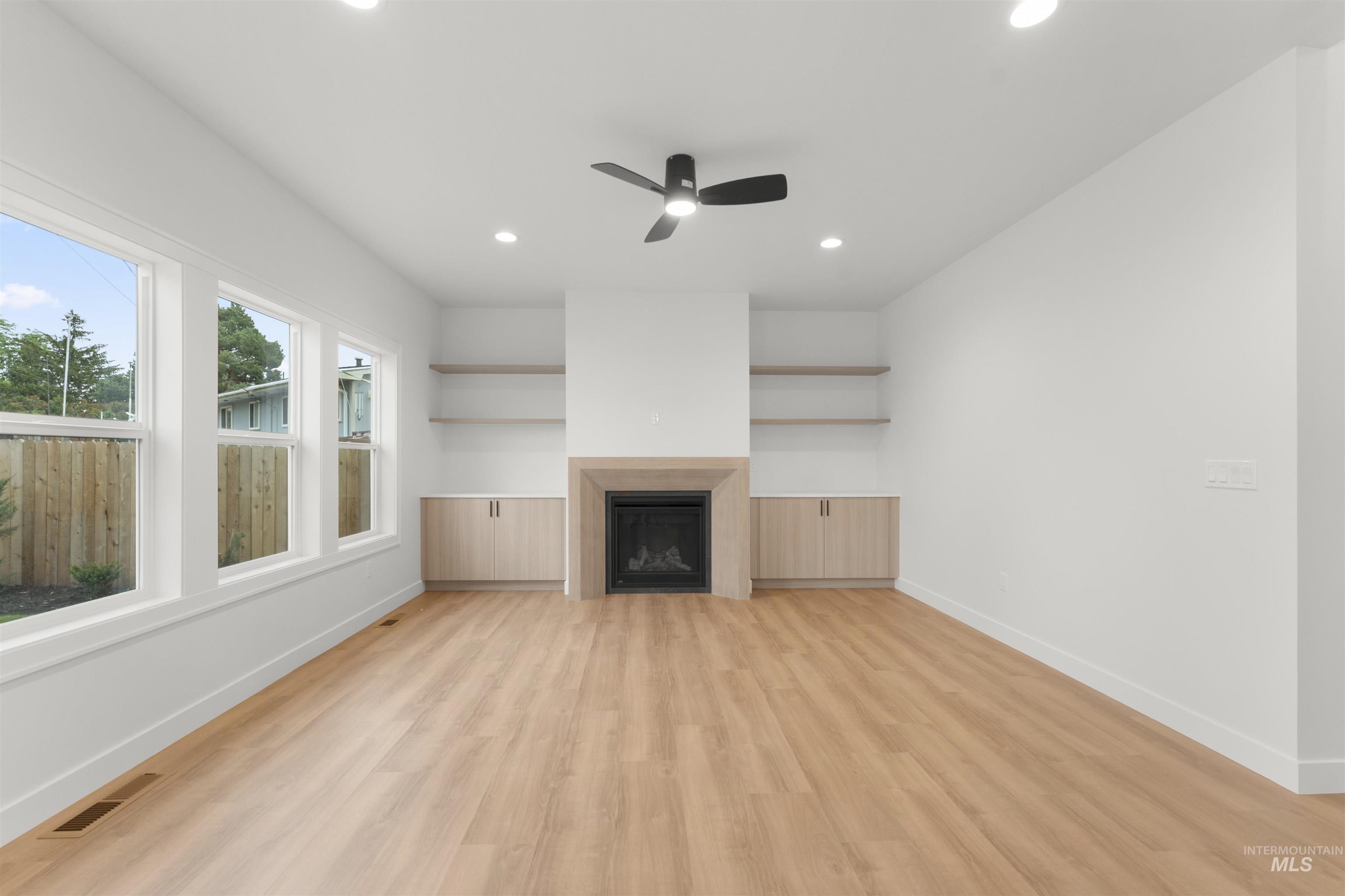 Unfurnished living room with light wood-style floors, a fireplace, recessed lighting, a ceiling fan, and built in shelves