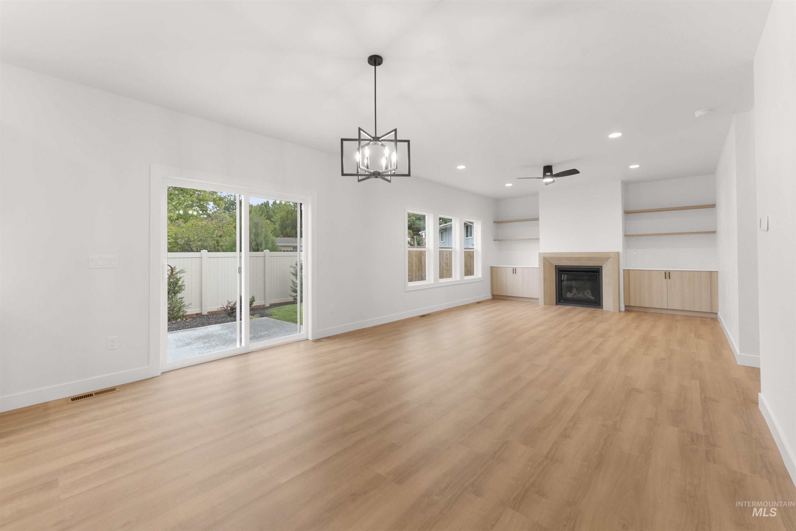 Unfurnished living room featuring light wood finished floors, a chandelier, recessed lighting, a glass covered fireplace, and a ceiling fan