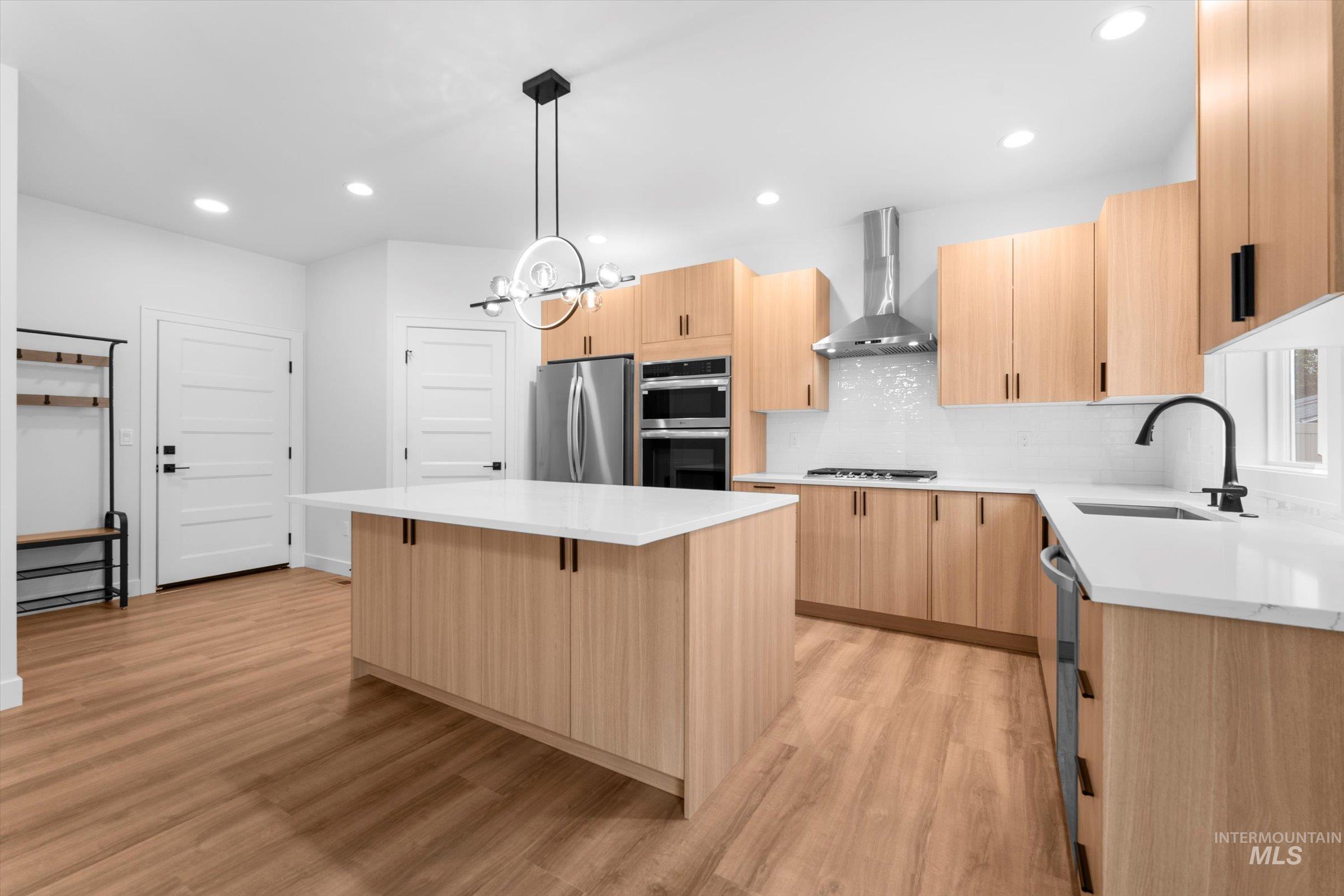 Kitchen featuring light brown cabinetry, decorative backsplash, light stone counters, decorative light fixtures, and recessed lighting