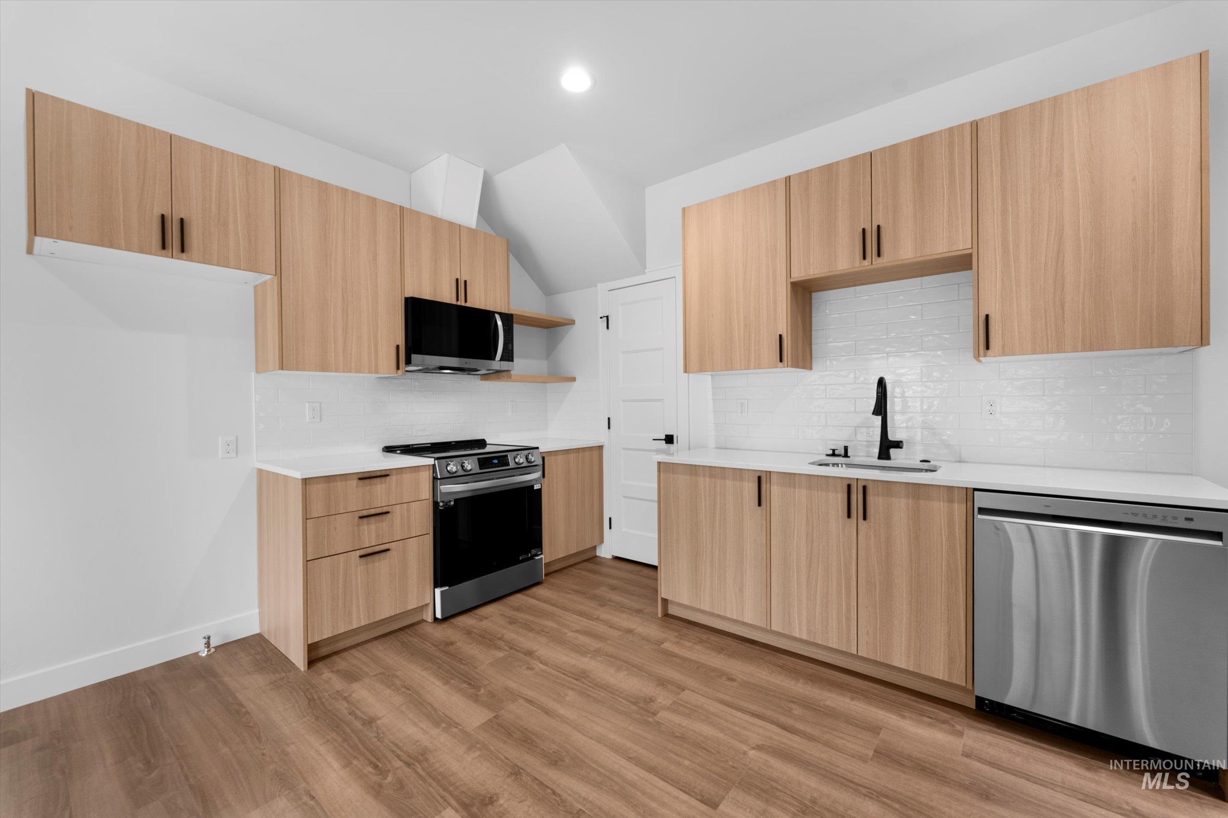 Kitchen featuring appliances with stainless steel finishes, tasteful backsplash, open shelves, modern cabinets, and vaulted ceiling