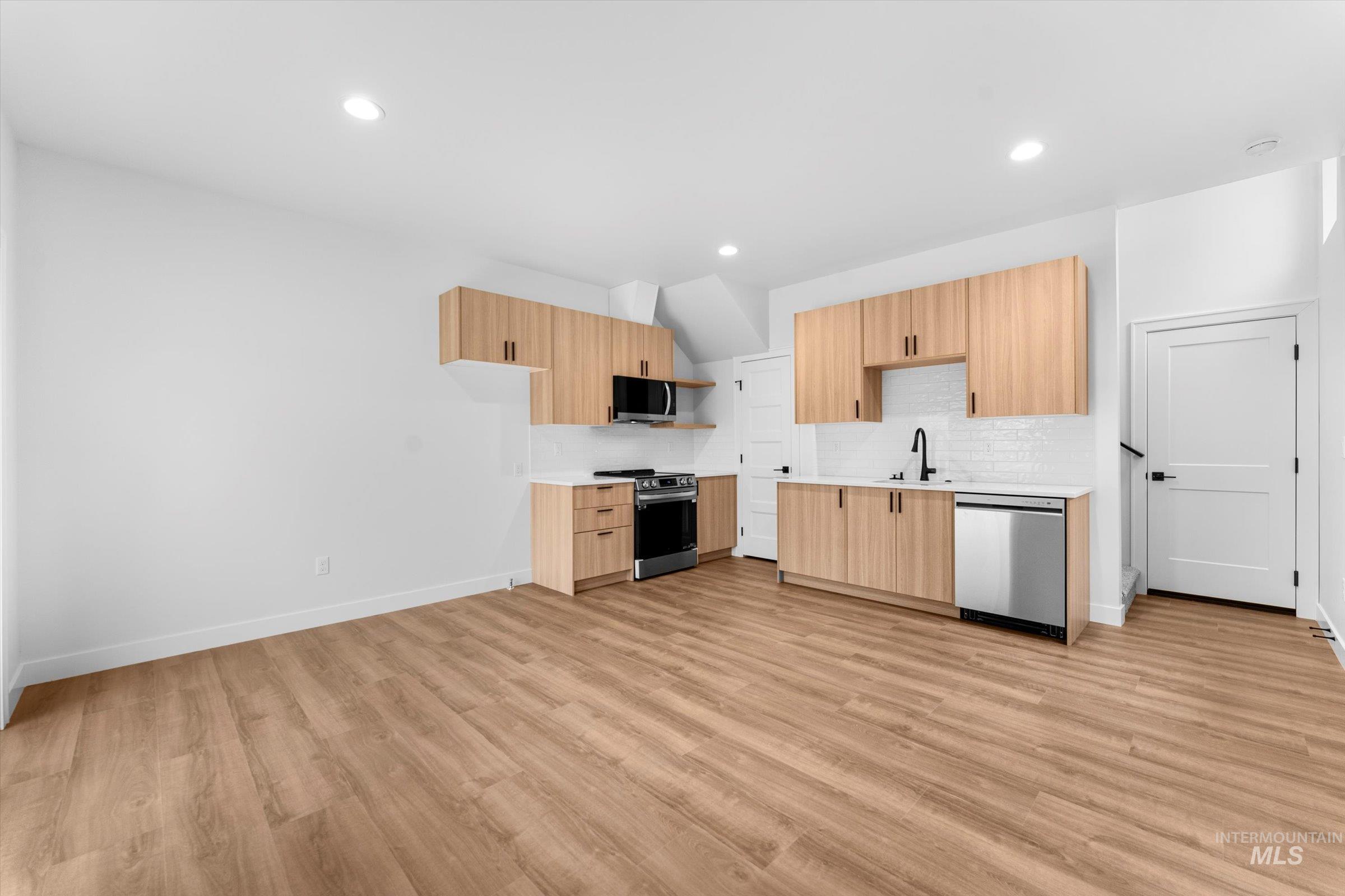 Kitchen with modern cabinets, decorative backsplash, stainless steel appliances, light brown cabinets, and light wood-type flooring