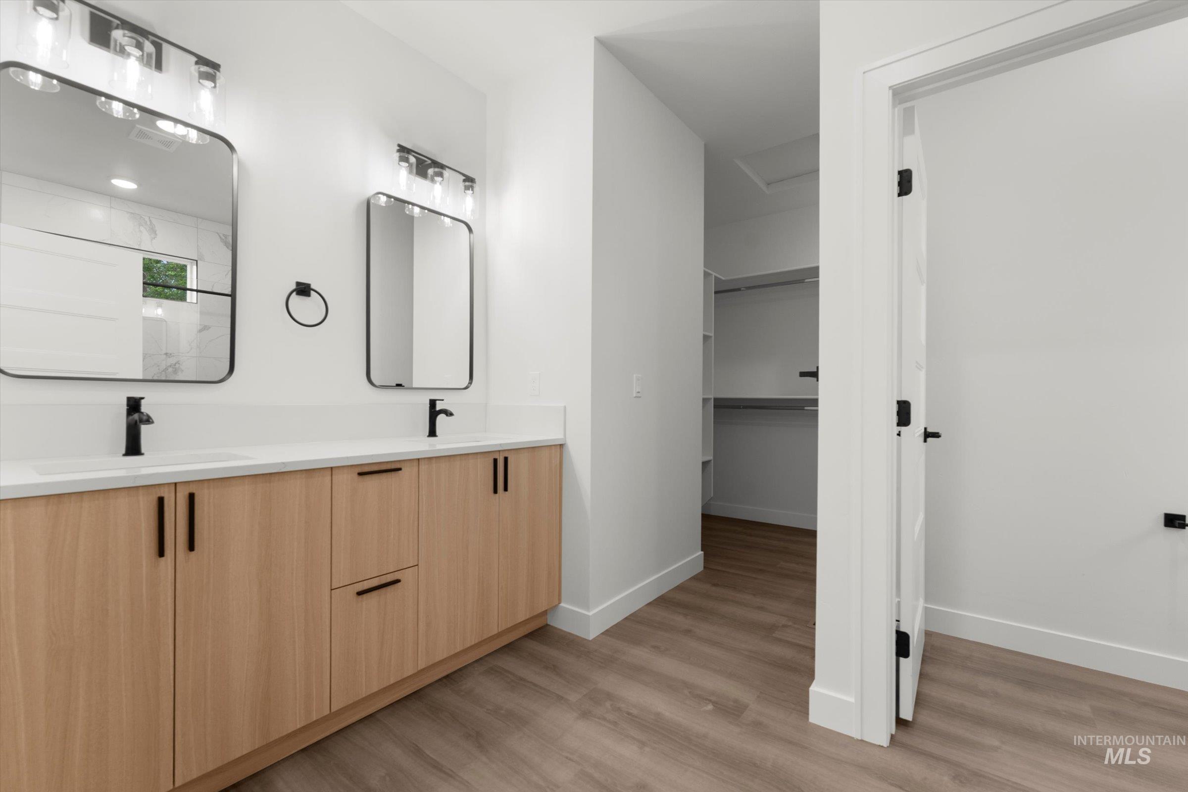 Bathroom featuring double vanity, light wood-style floors, and a spacious closet