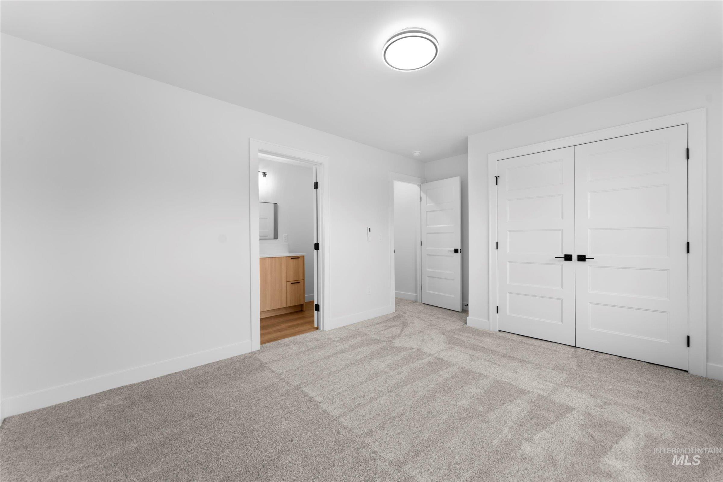 Unfurnished bedroom featuring light colored carpet, a closet, and ensuite bath