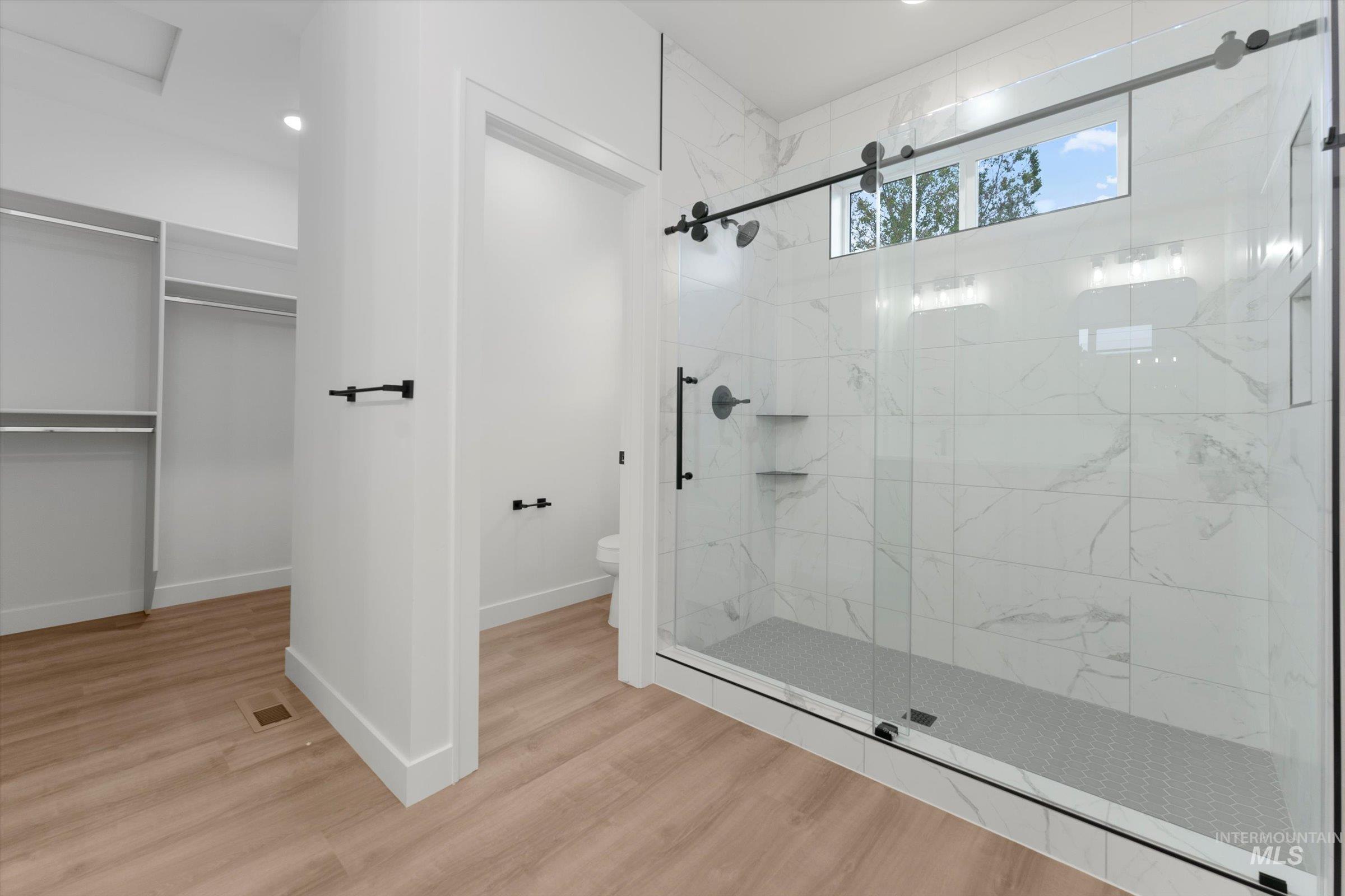 Full bath with a marble finish shower, wood finished floors, a walk in closet, and recessed lighting