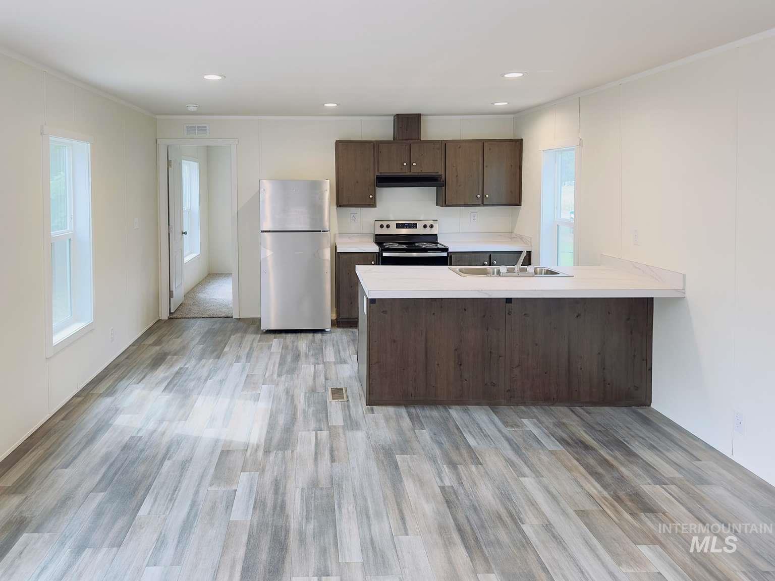 Kitchen featuring dark brown cabinets, light countertops, appliances with stainless steel finishes, a peninsula, and crown molding