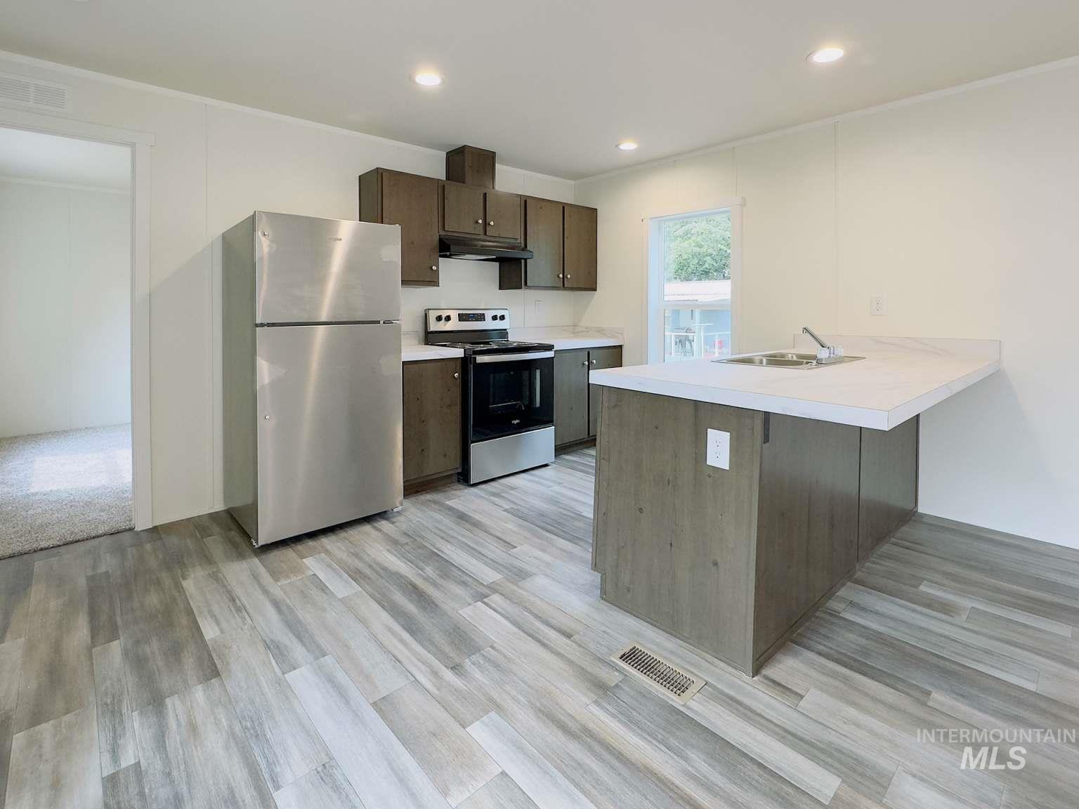 Kitchen featuring appliances with stainless steel finishes, light countertops, a kitchen breakfast bar, a peninsula, and dark brown cabinets