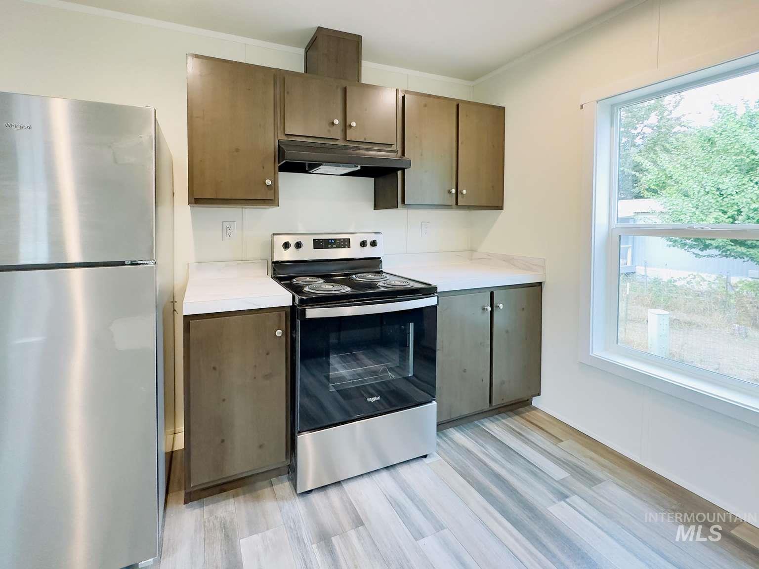 Kitchen featuring appliances with stainless steel finishes, light countertops, under cabinet range hood, light wood-type flooring, and ornamental molding