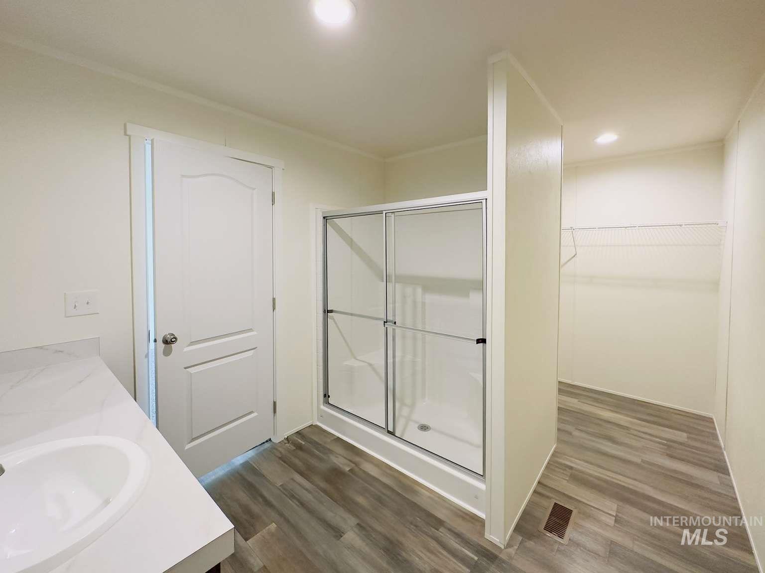 Bathroom with a shower stall, dark wood-type flooring, double vanity, a walk in closet, and recessed lighting