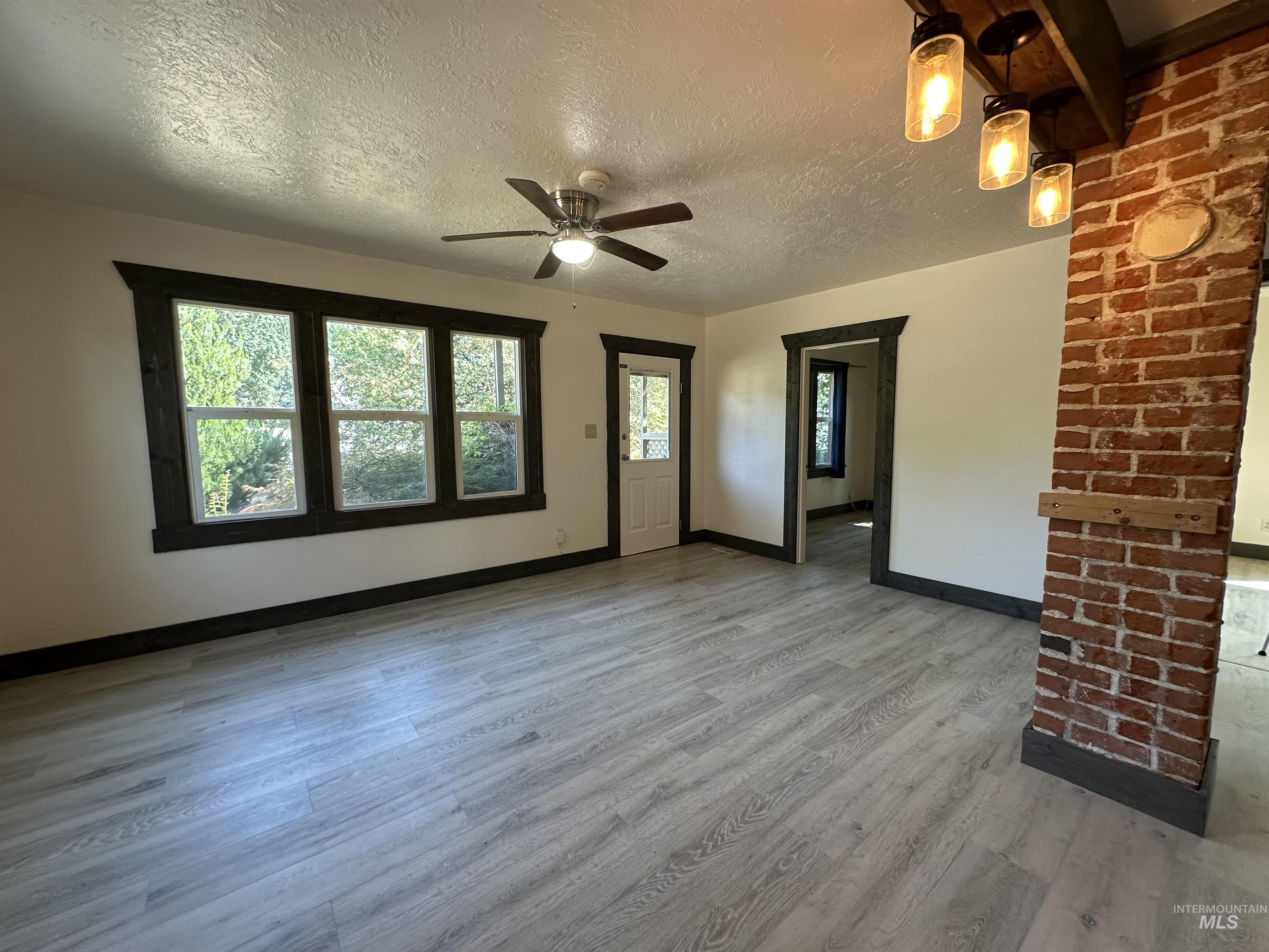 Unfurnished living room featuring a textured ceiling, light wood-style floors, and a ceiling fan