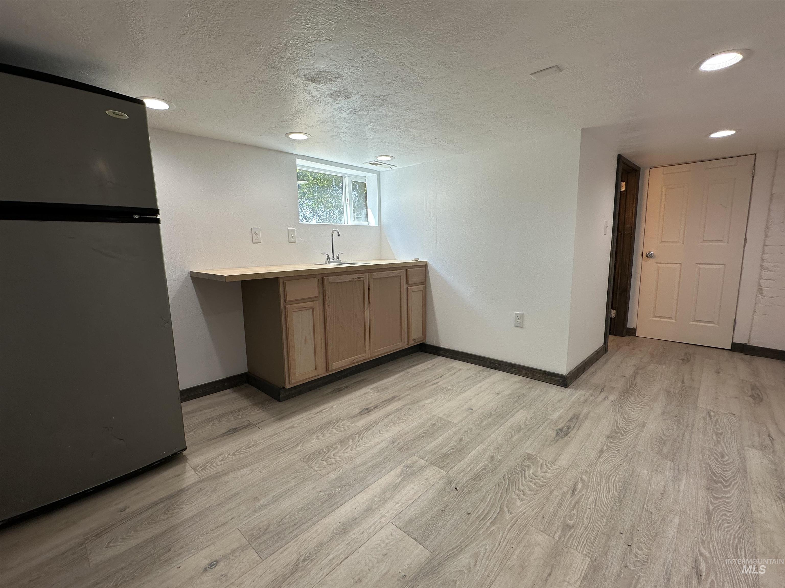 Kitchen featuring freestanding refrigerator, light wood-style flooring, a textured ceiling, light countertops, and recessed lighting
