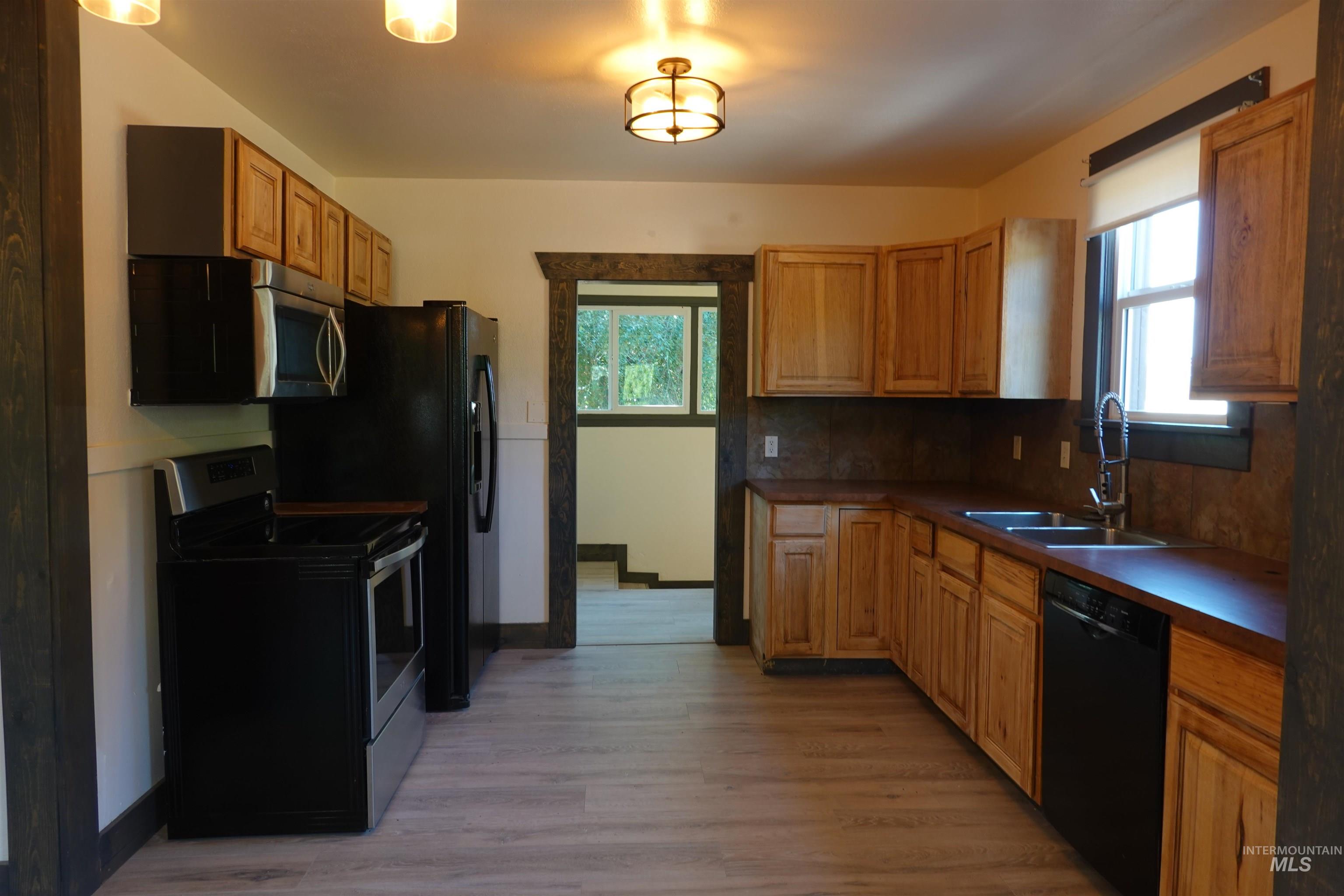 Kitchen with appliances with stainless steel finishes, decorative backsplash, light wood-style flooring, and dark countertops