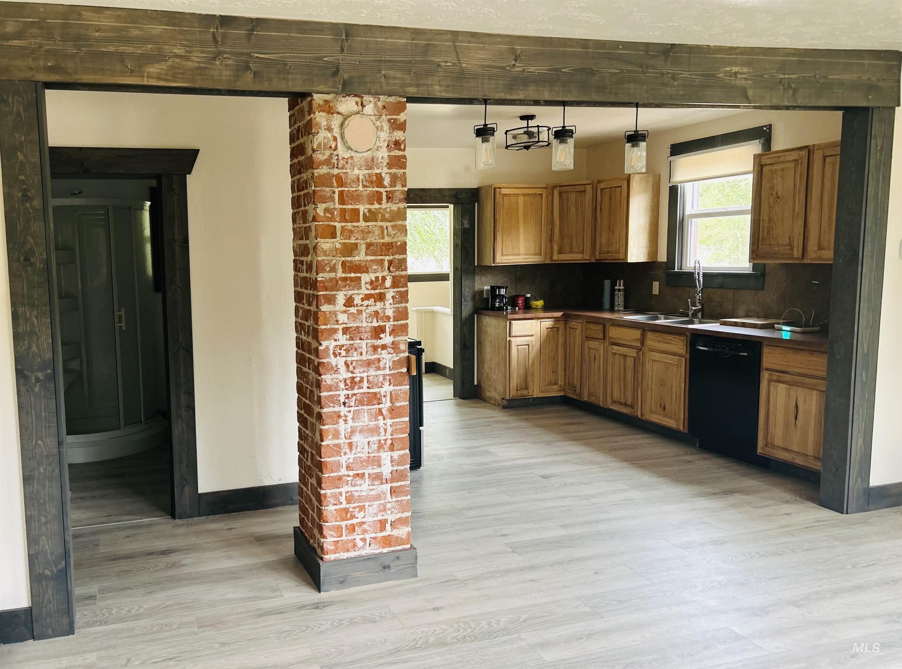 Kitchen with dark countertops, light wood finished floors, black dishwasher, brown cabinets, and decorative light fixtures