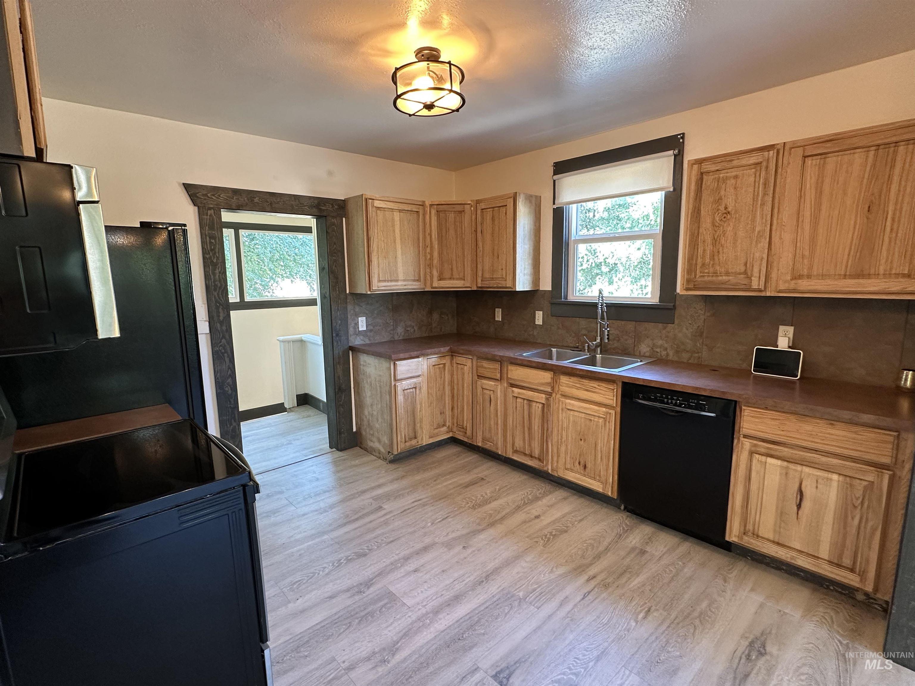 Kitchen featuring black appliances, decorative backsplash, dark countertops, and light wood-style flooring