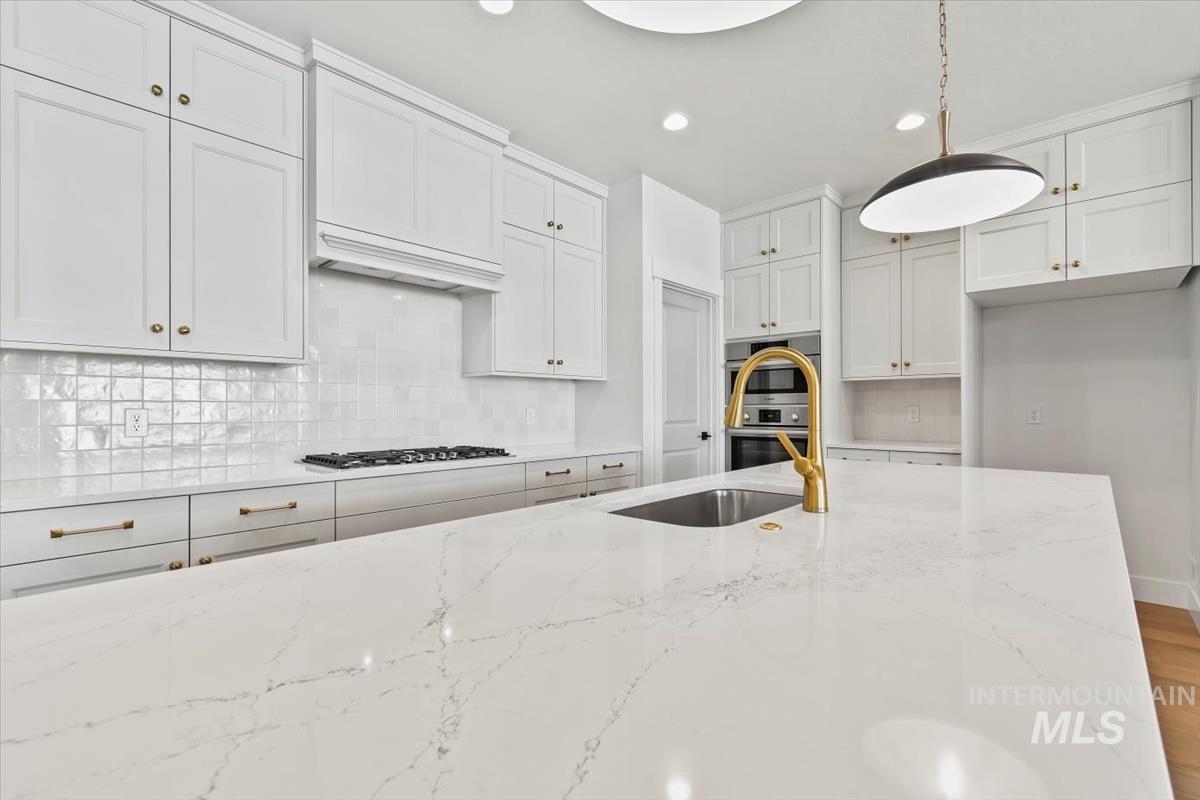 Kitchen featuring light stone counters, backsplash, white cabinetry, and recessed lighting