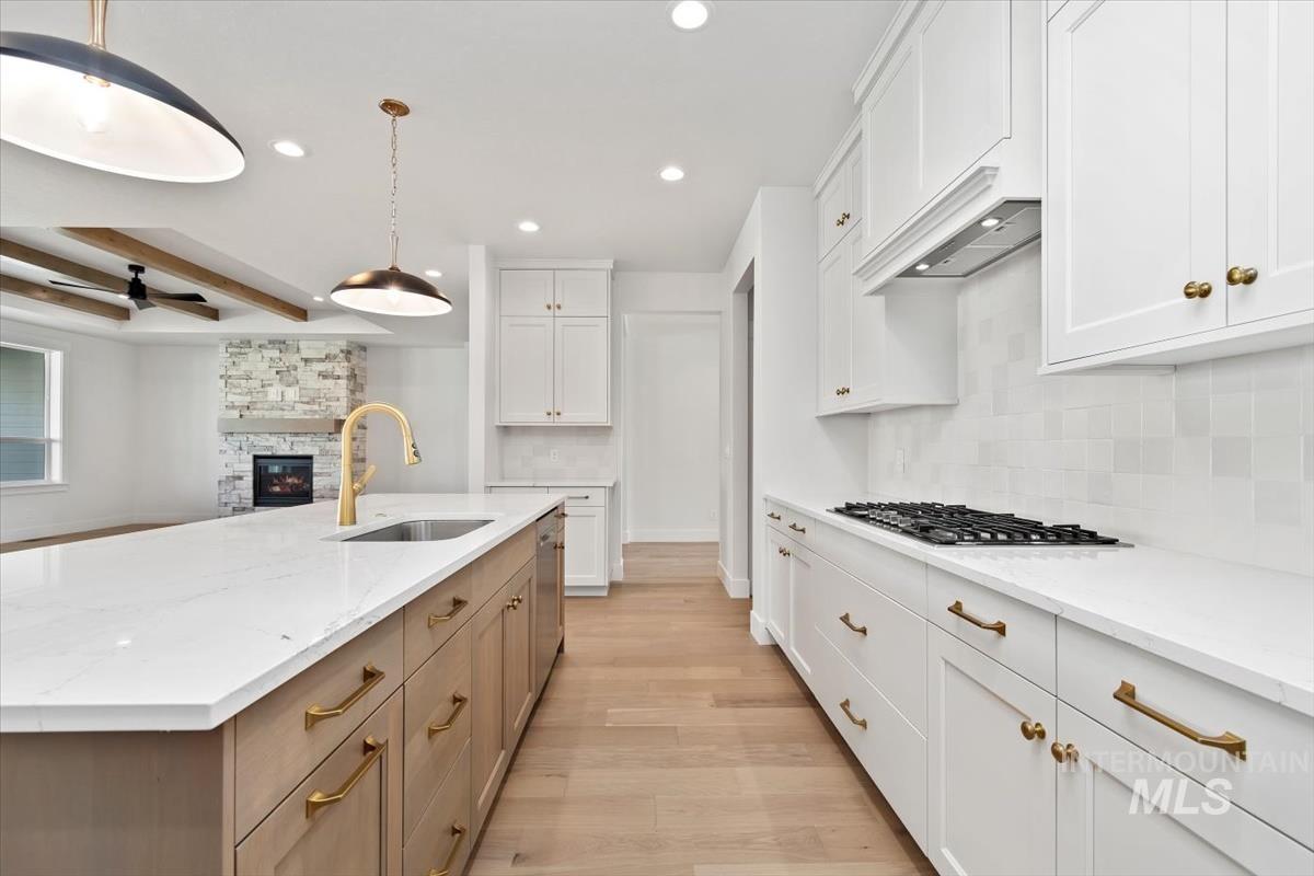 Kitchen featuring white cabinetry, beamed ceiling, recessed lighting, light wood-style floors, and a stone fireplace
