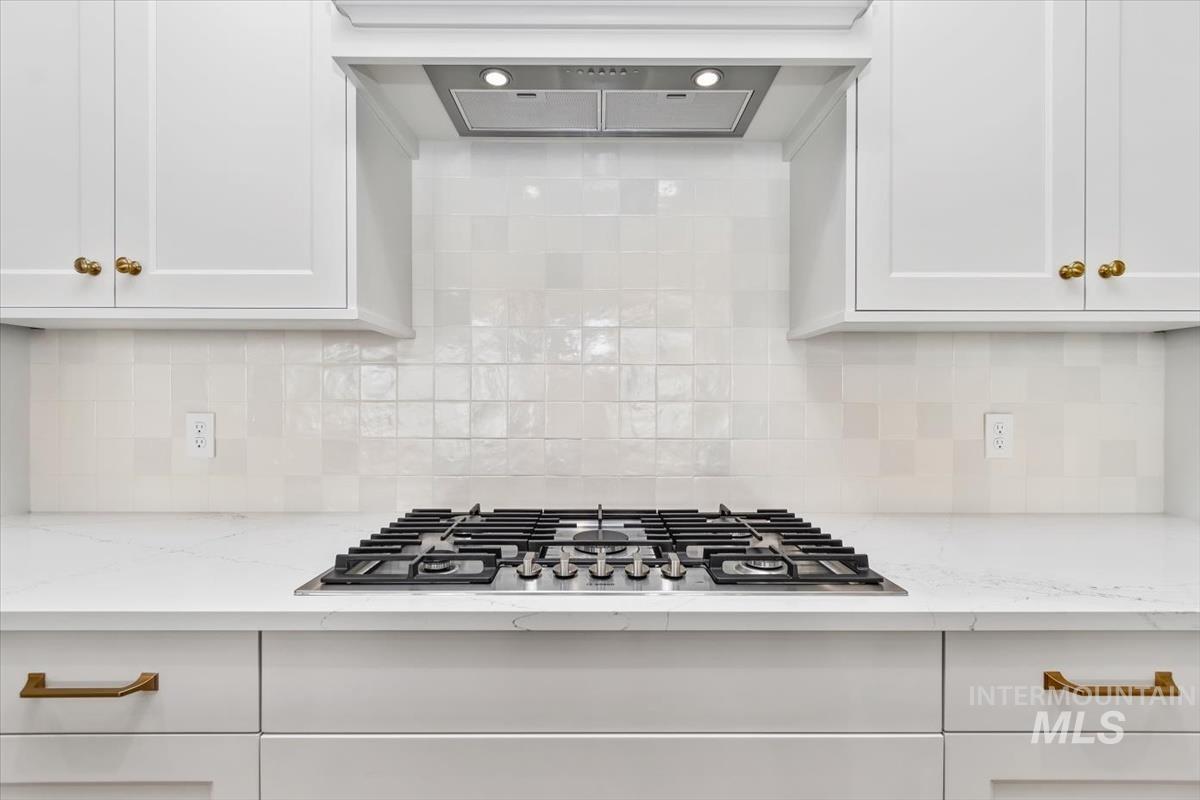 Kitchen featuring ventilation hood, light stone countertops, and white cabinetry