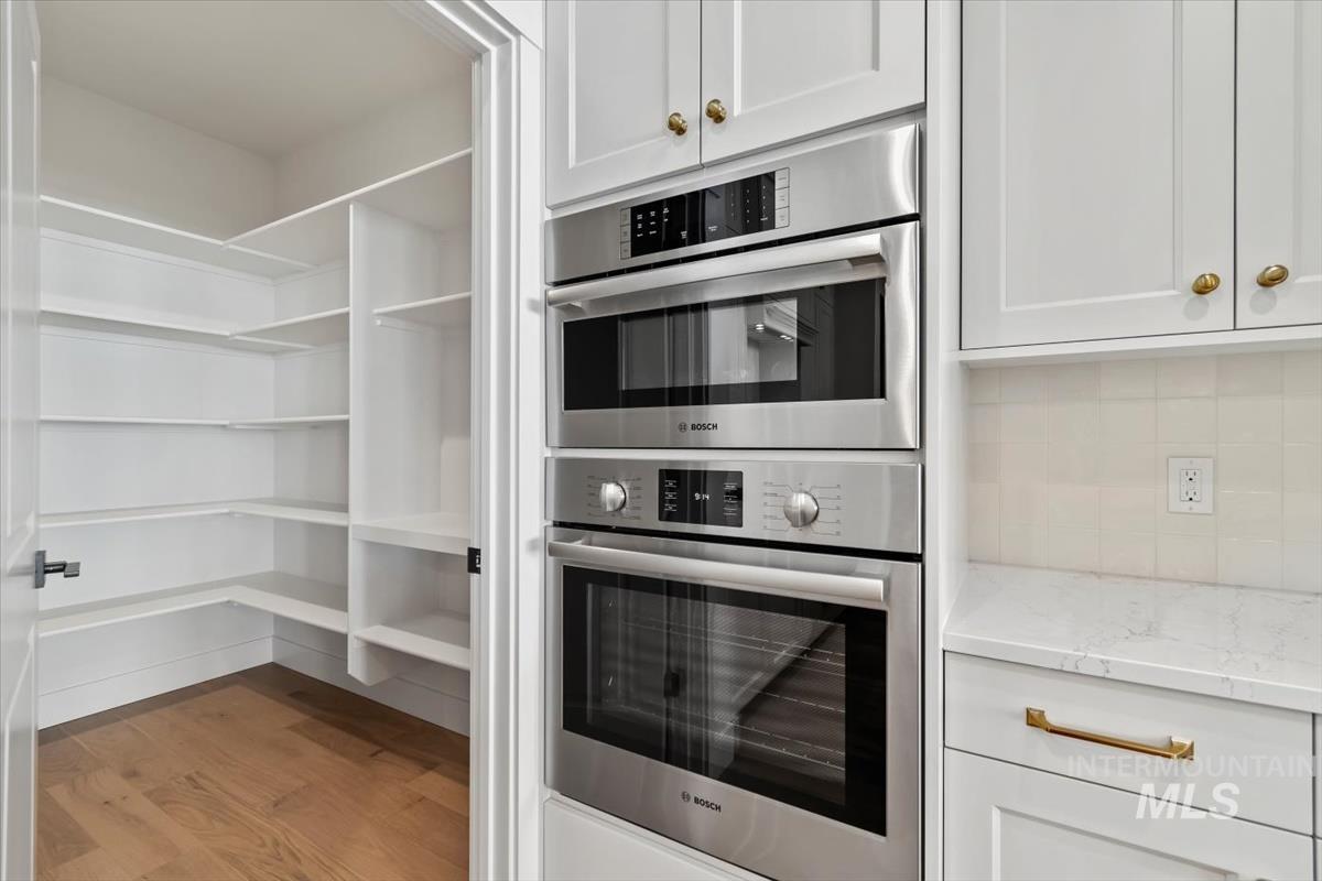 Kitchen with stainless steel double oven, light wood-style flooring, white cabinetry, and light stone counters
