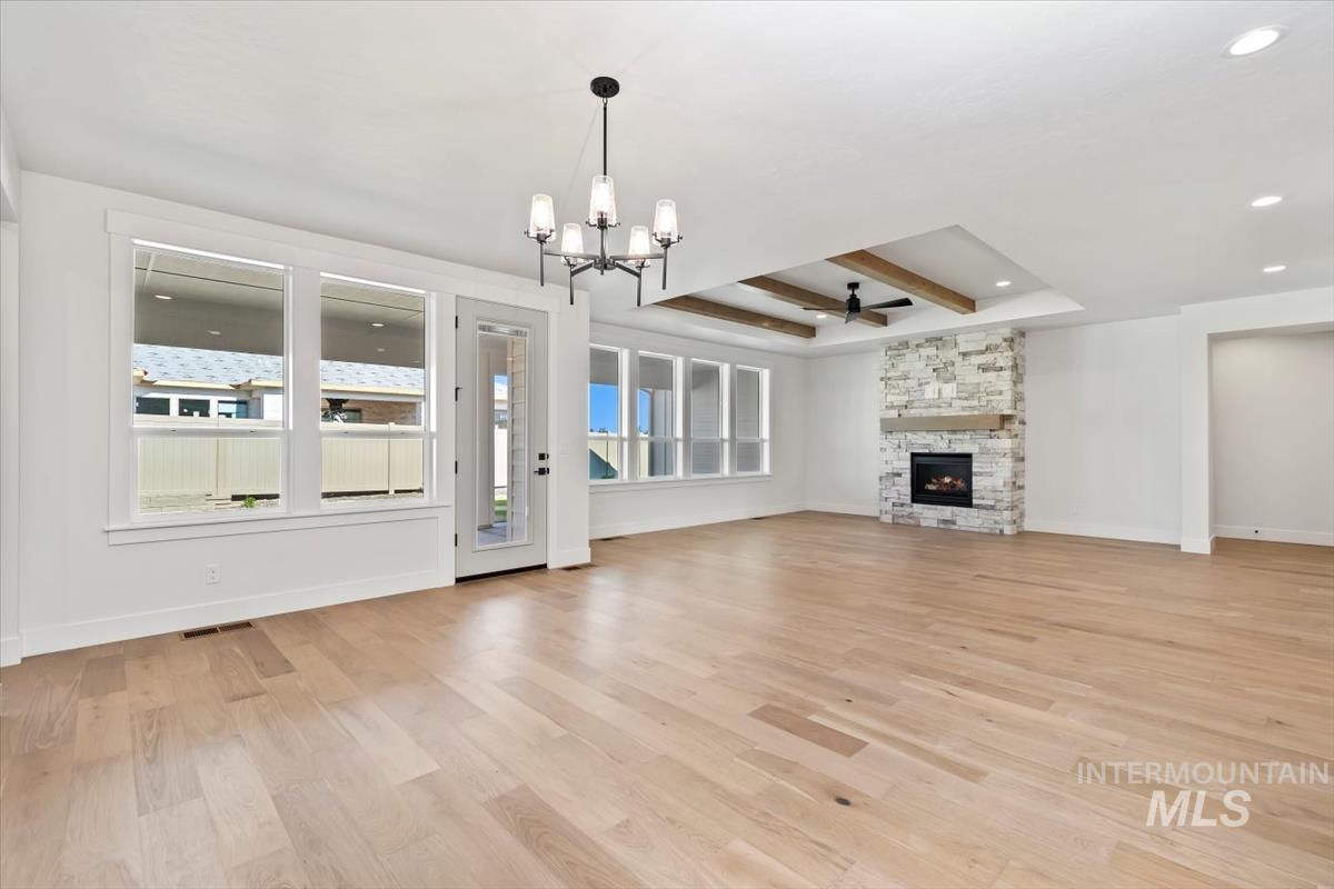 Unfurnished living room featuring a chandelier, light wood-style flooring, a raised ceiling, a fireplace, and ceiling fan