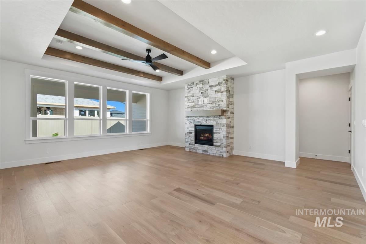 Unfurnished living room with a tray ceiling, a ceiling fan, light wood-type flooring, a fireplace, and beamed ceiling