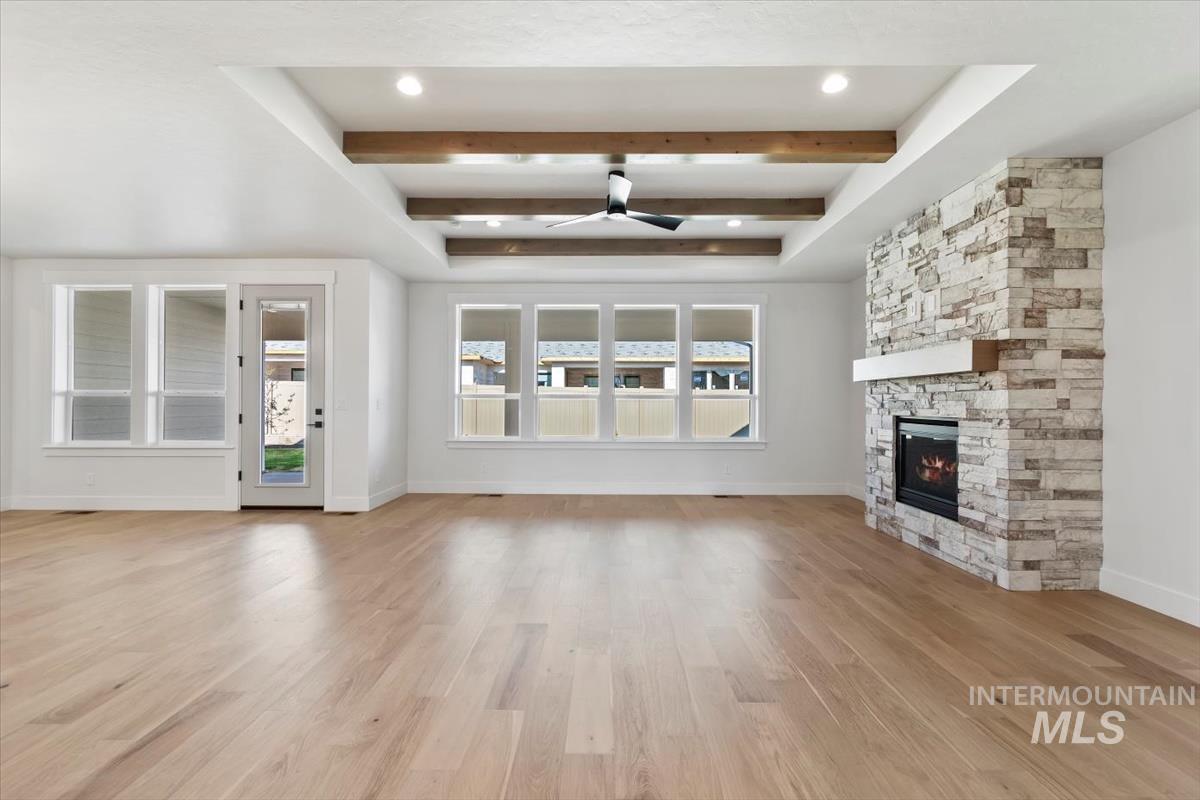 Unfurnished living room featuring beamed ceiling, light wood-style flooring, a fireplace, and a ceiling fan