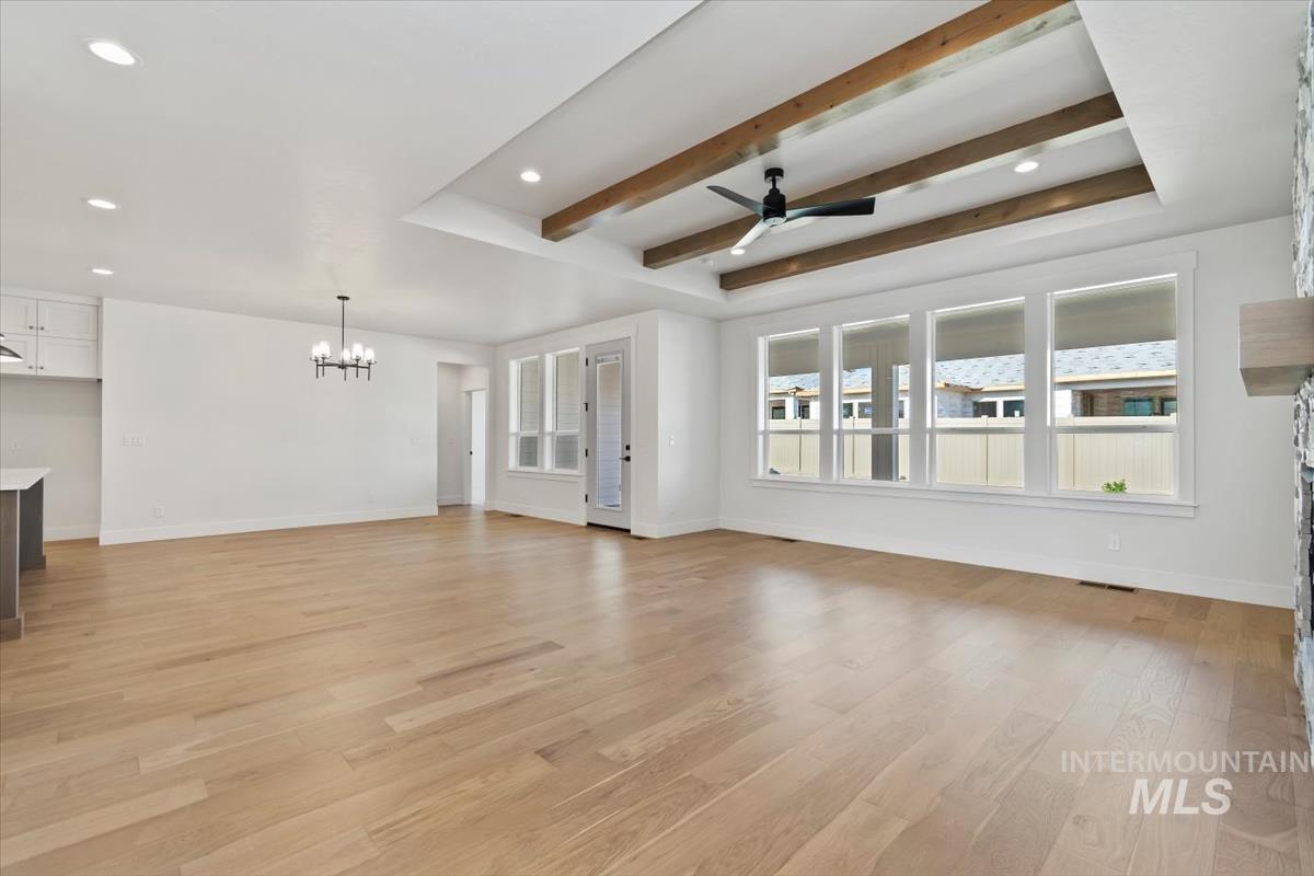 Unfurnished living room with beamed ceiling, light wood finished floors, recessed lighting, ceiling fan, and a chandelier