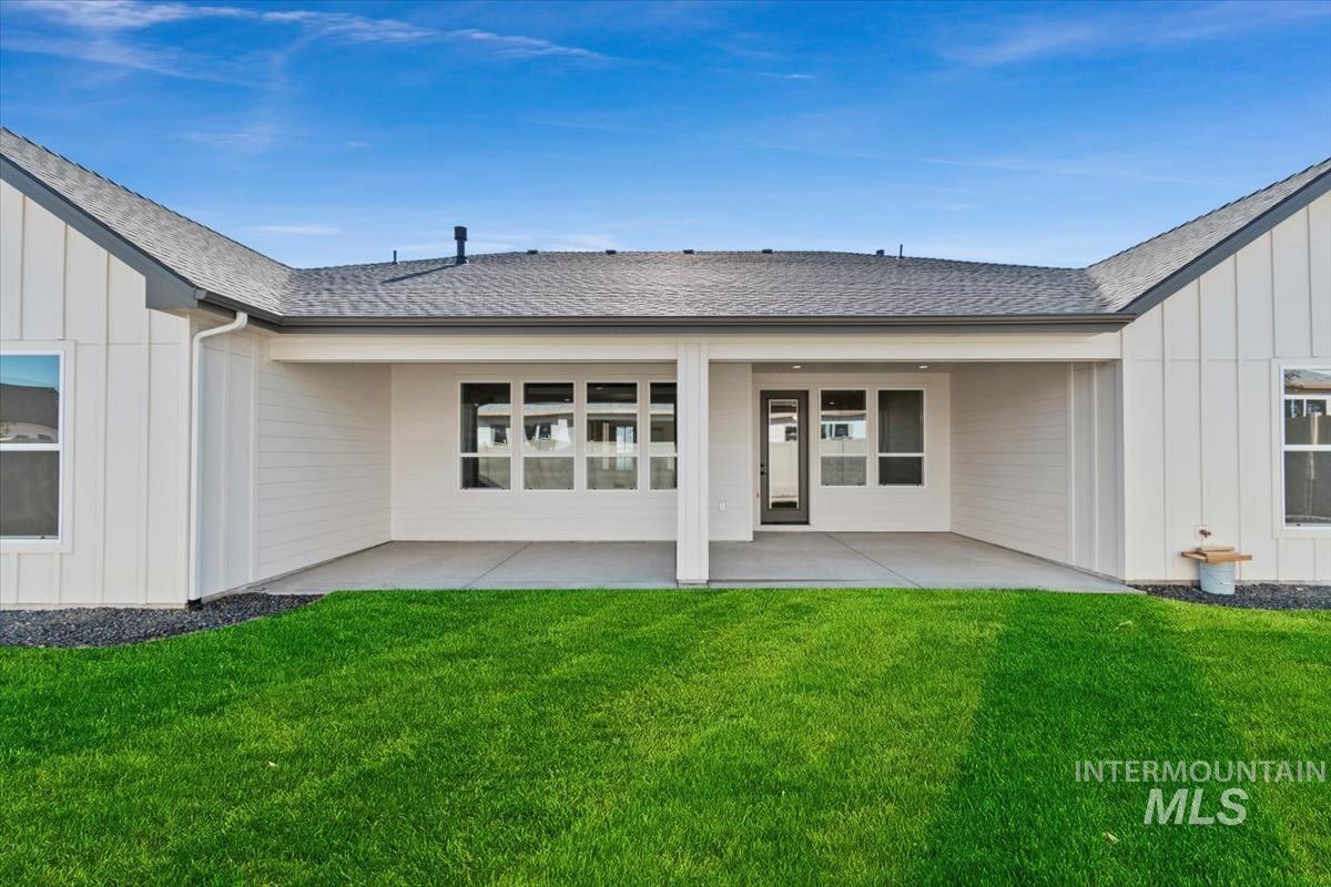 Back of house featuring roof with shingles, board and batten siding, a patio, and a yard