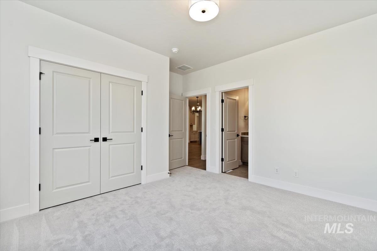 Unfurnished bedroom with carpet, a closet, connected bathroom, and a chandelier