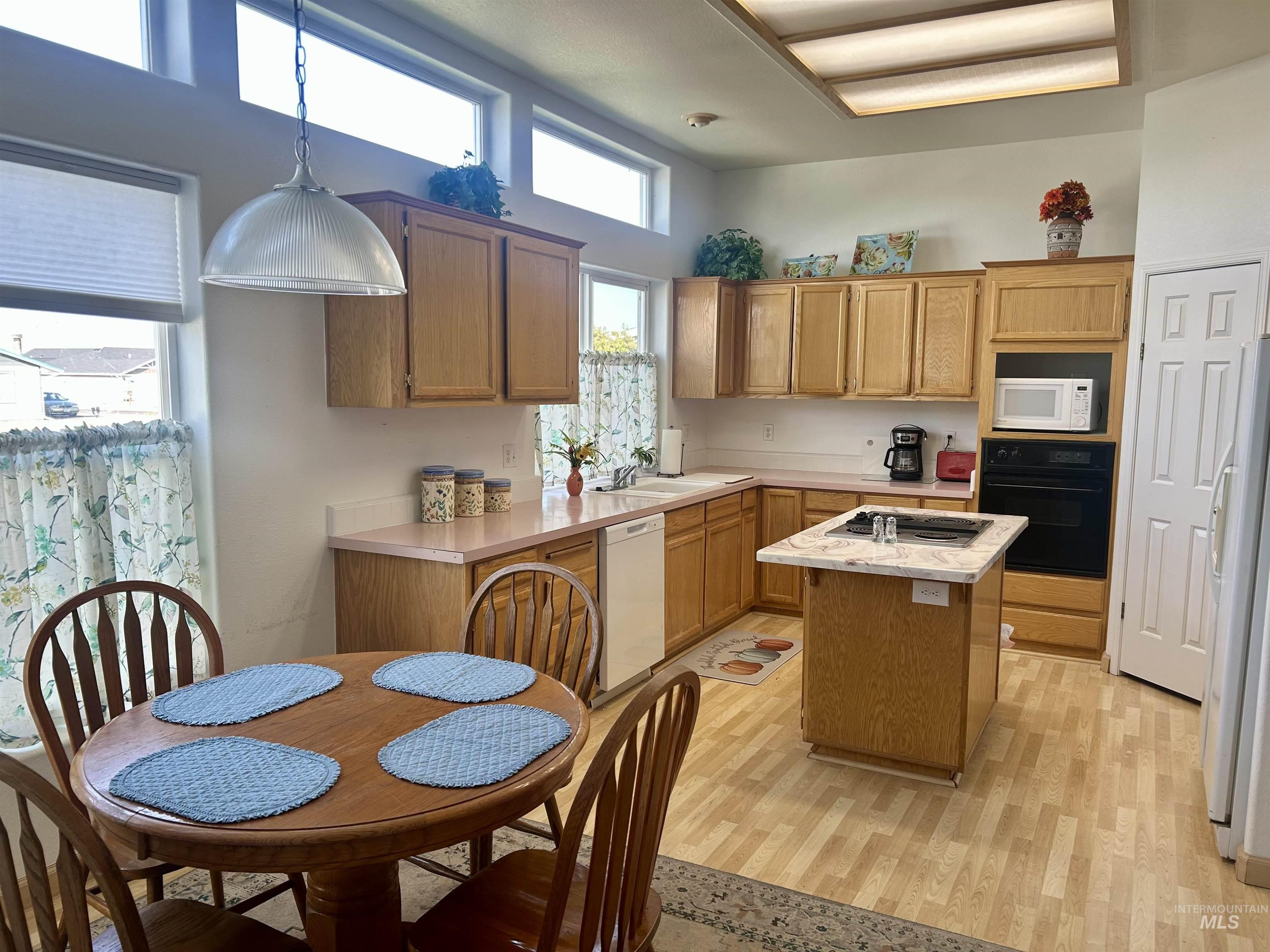 Kitchen featuring light countertops, white appliances, a kitchen island, and light wood-type flooring
