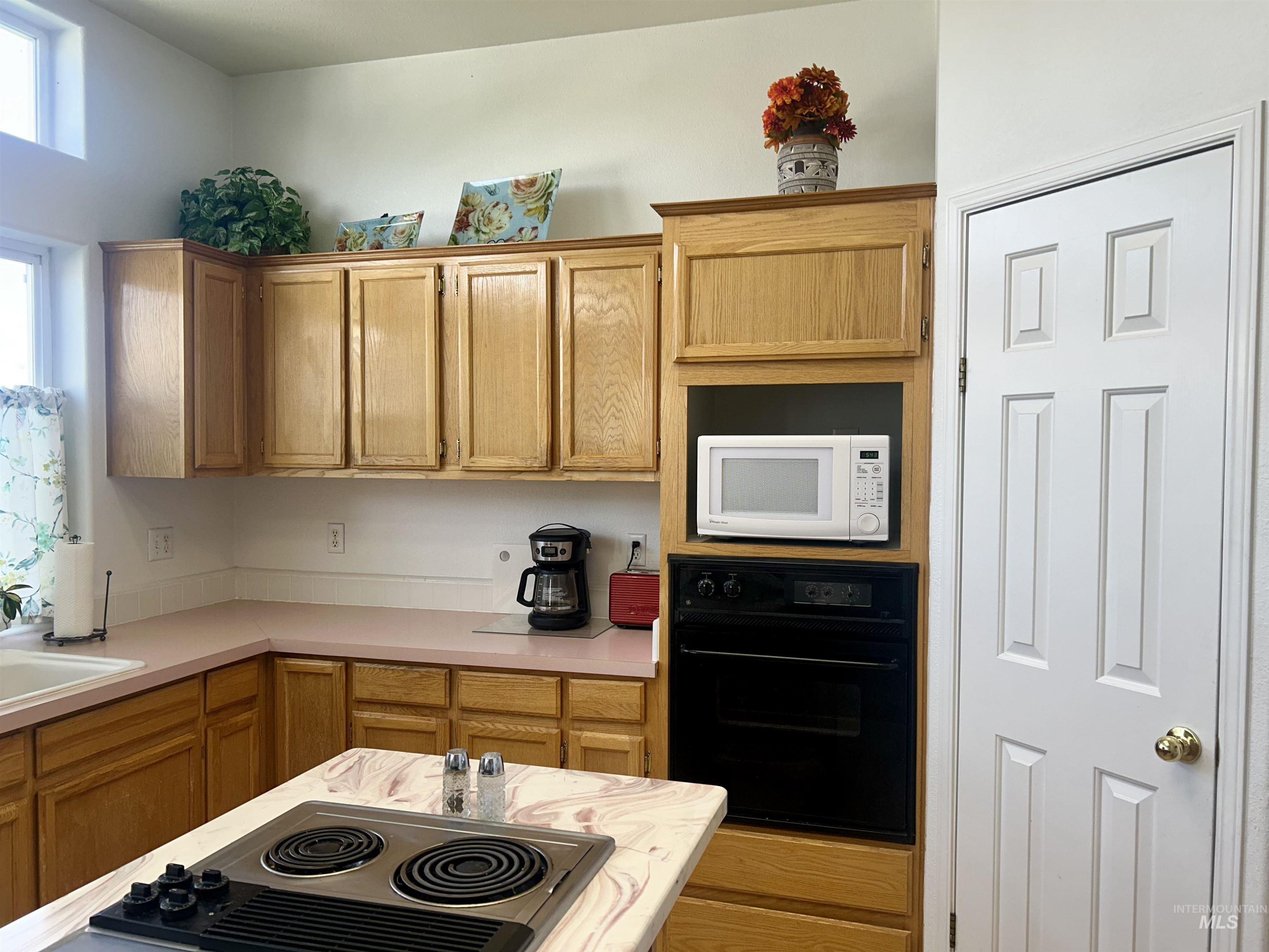 Kitchen with oven, light countertops, white microwave, stainless steel electric cooktop, and brown cabinets
