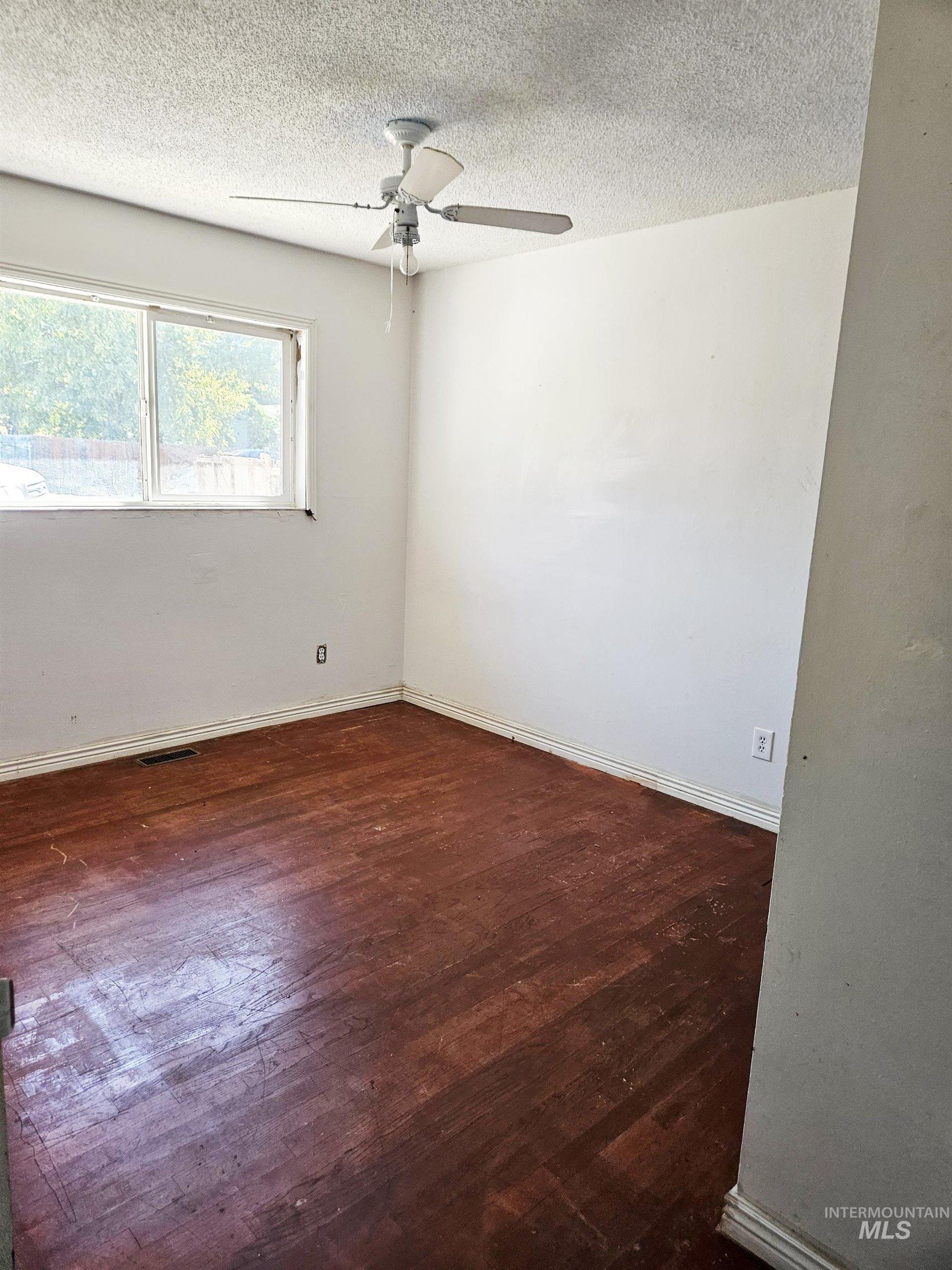 Empty room with dark wood finished floors, a textured ceiling, and a ceiling fan