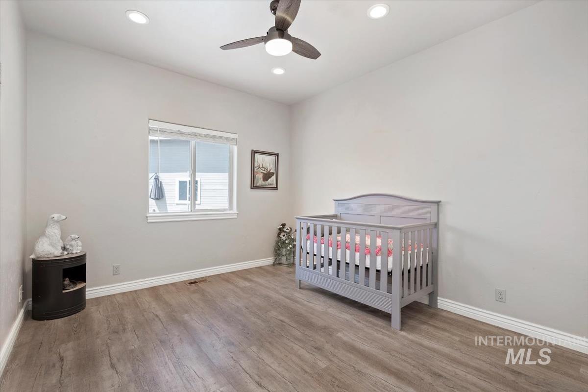Bedroom with a nursery area, light wood-style flooring, recessed lighting, and a ceiling fan