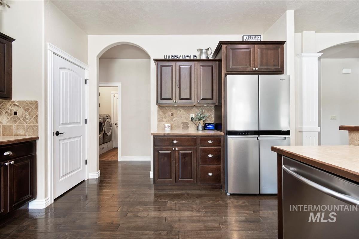 Kitchen featuring arched walkways, appliances with stainless steel finishes, light countertops, dark brown cabinetry, and dark wood-type flooring
