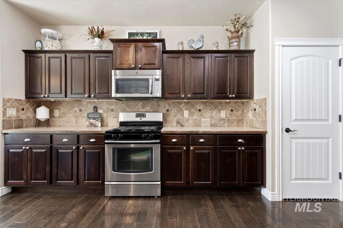 Kitchen with appliances with stainless steel finishes, dark brown cabinetry, dark wood-style floors, and tasteful backsplash