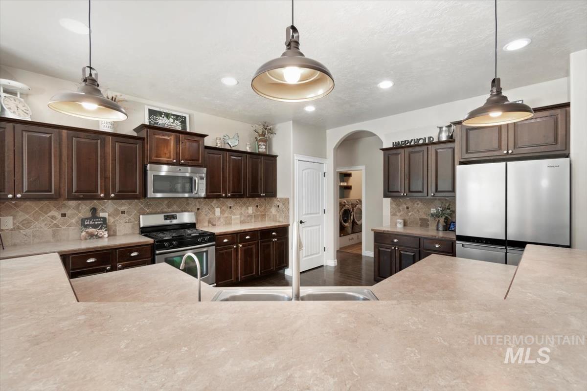 Kitchen with dark brown cabinetry, appliances with stainless steel finishes, light countertops, decorative light fixtures, and recessed lighting