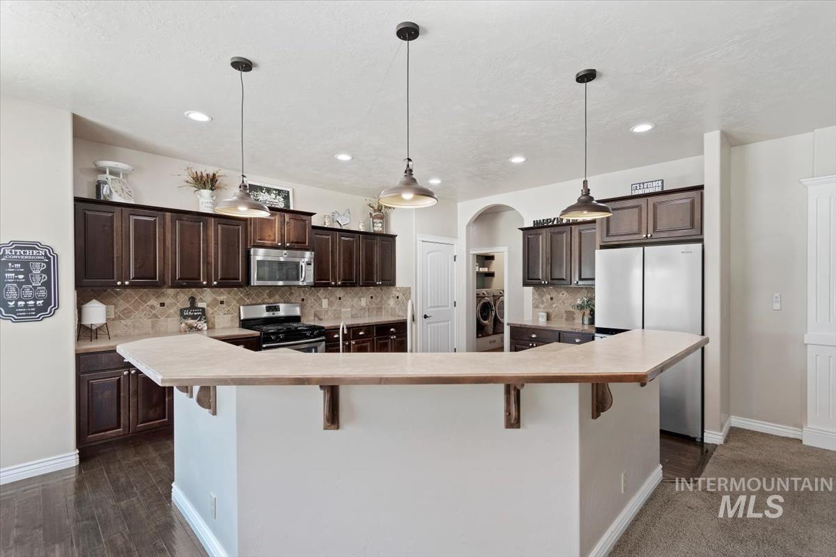 Kitchen with light countertops, appliances with stainless steel finishes, tasteful backsplash, dark brown cabinets, and arched walkways