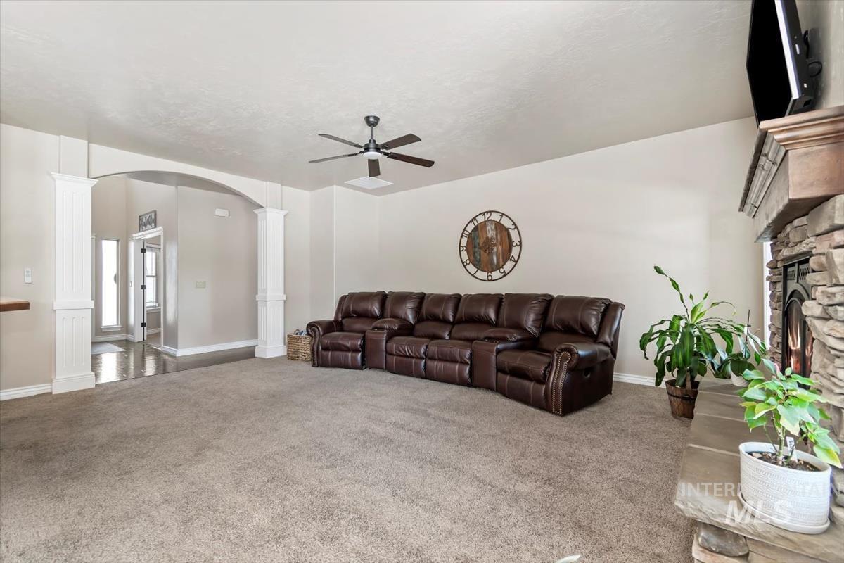 Living room with carpet, arched walkways, a stone fireplace, and ceiling fan