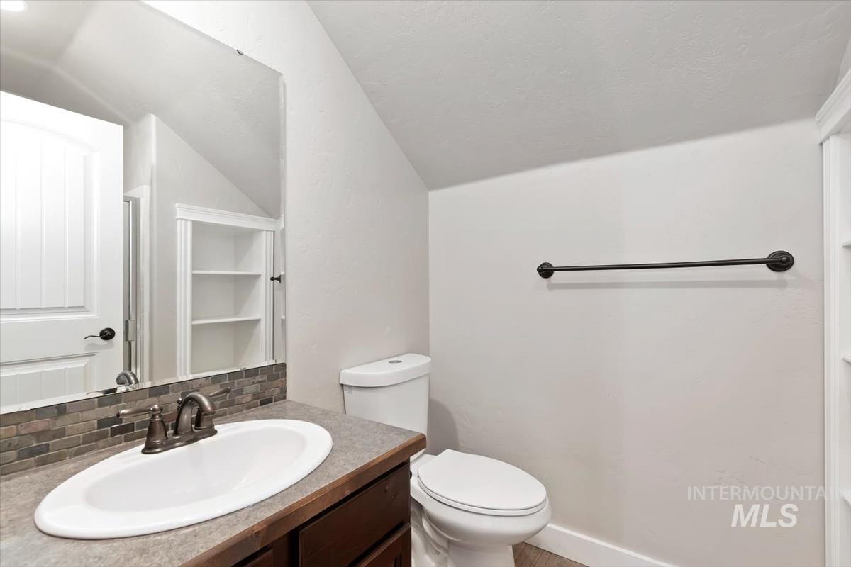 Bathroom with decorative backsplash, vanity, vaulted ceiling, and a textured ceiling
