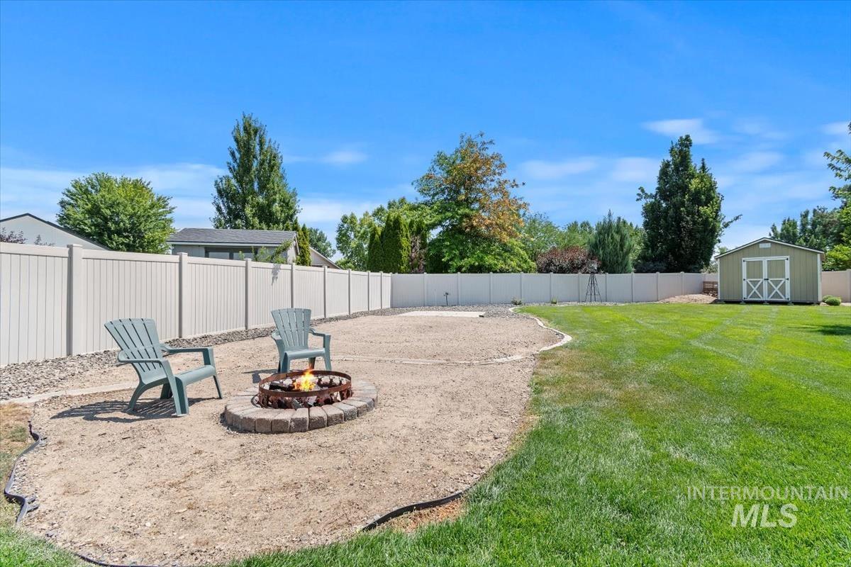 Fenced backyard featuring a storage unit, an outdoor fire pit, and a patio