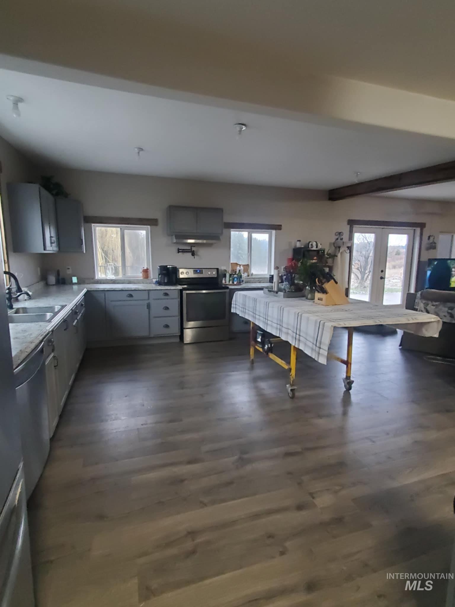 Kitchen featuring gray cabinets, light countertops, appliances with stainless steel finishes, healthy amount of natural light, and beamed ceiling