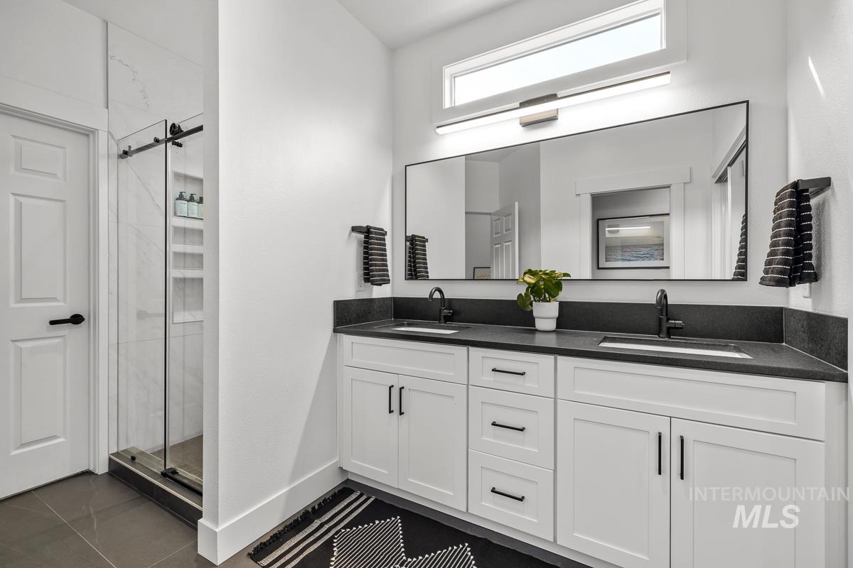 Bathroom with a shower stall, double vanity, and dark tile patterned floors