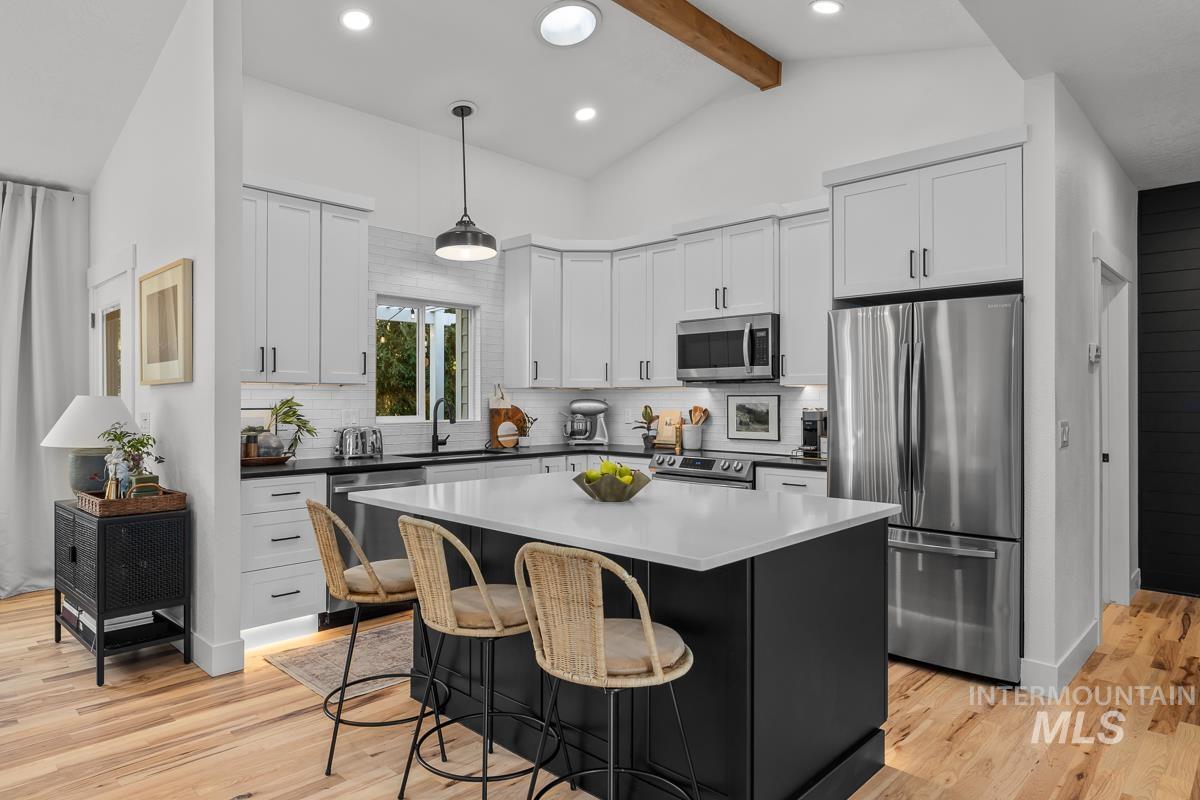 Kitchen featuring appliances with stainless steel finishes, dark cabinets, backsplash, light wood finished floors, and hanging light fixtures