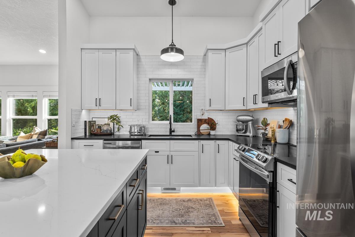Kitchen featuring appliances with stainless steel finishes, light wood-style flooring, hanging light fixtures, dark stone counters, and tasteful backsplash