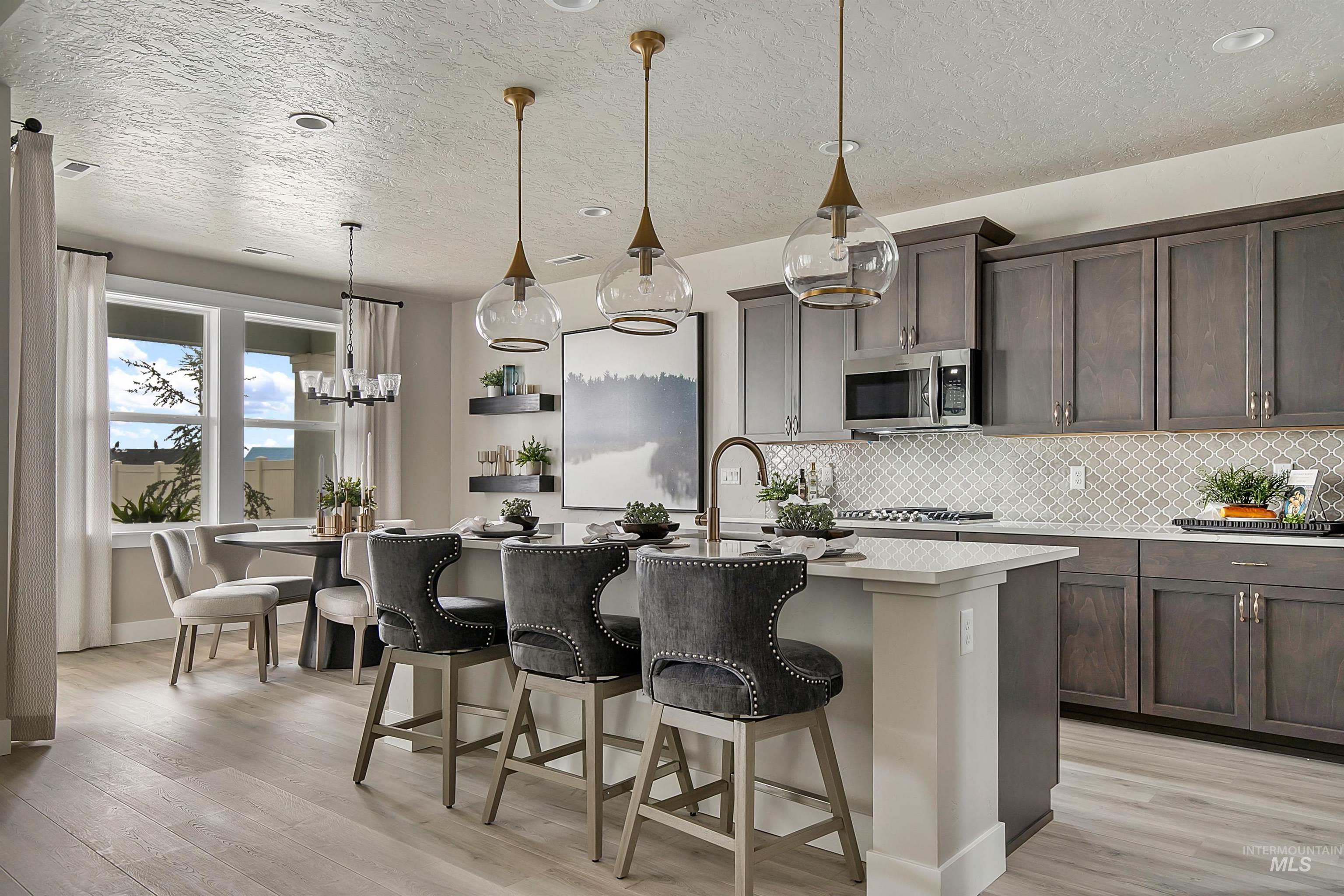 Kitchen featuring decorative backsplash, hanging light fixtures, a breakfast bar, light wood-type flooring, and a textured ceiling