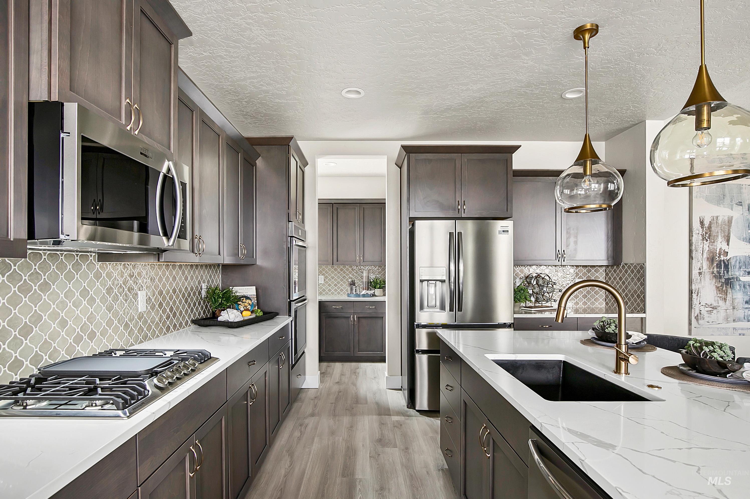 Kitchen featuring light wood-style flooring, stainless steel appliances, decorative light fixtures, backsplash, and a textured ceiling