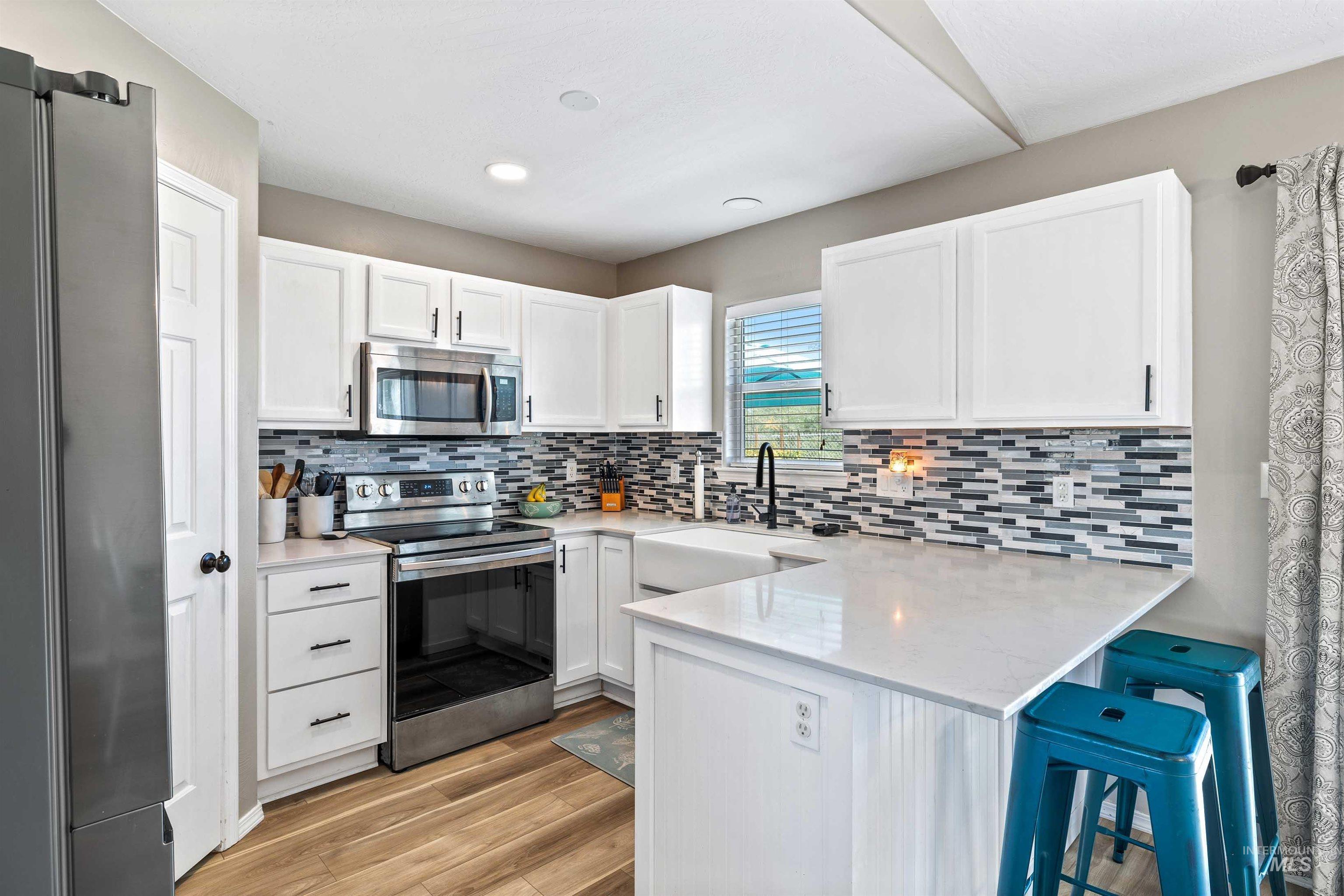 Kitchen featuring appliances with stainless steel finishes, white cabinets, a kitchen breakfast bar, tasteful backsplash, and light wood-style floors