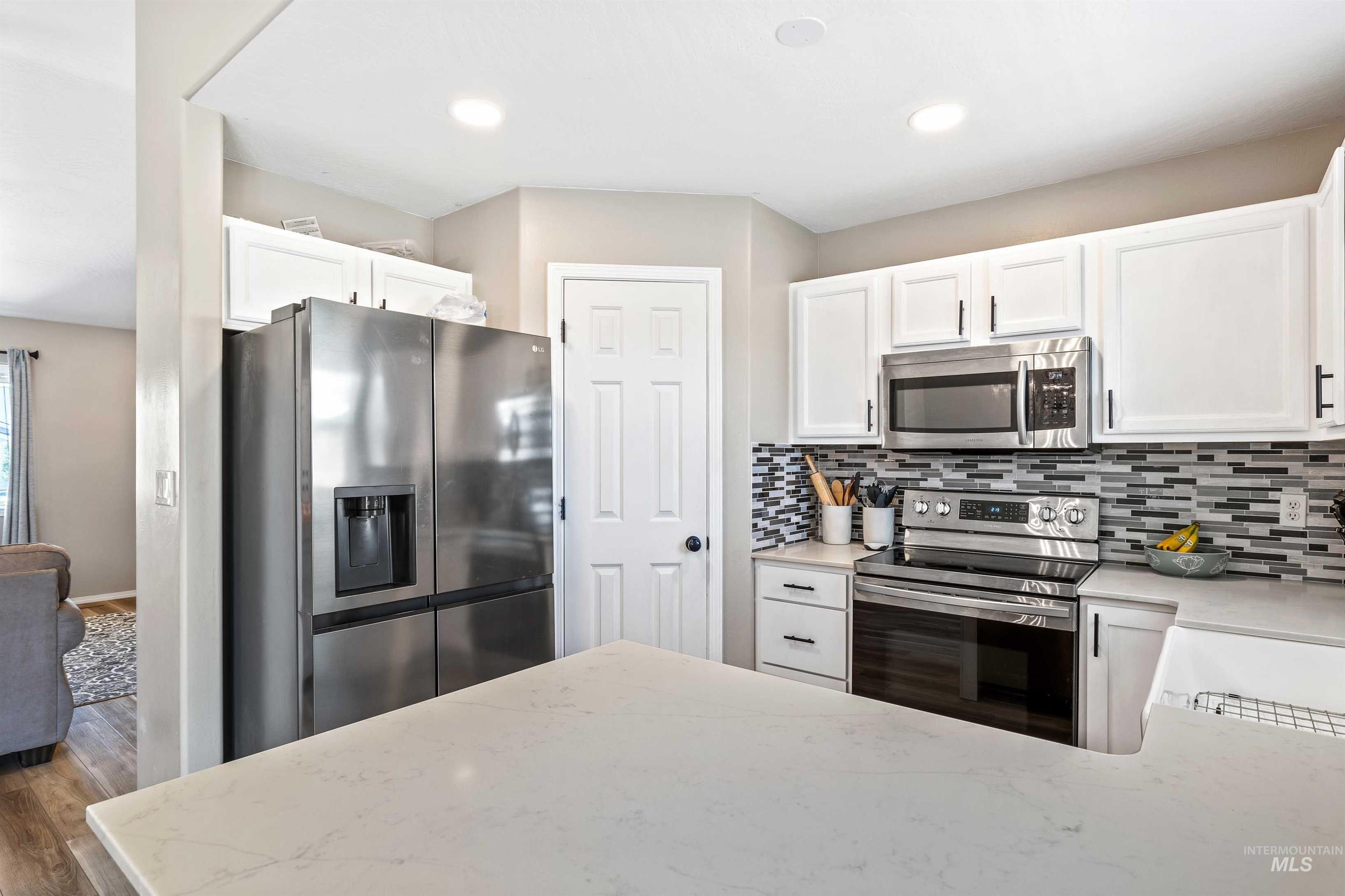 Kitchen with appliances with stainless steel finishes, white cabinets, tasteful backsplash, light stone countertops, and recessed lighting