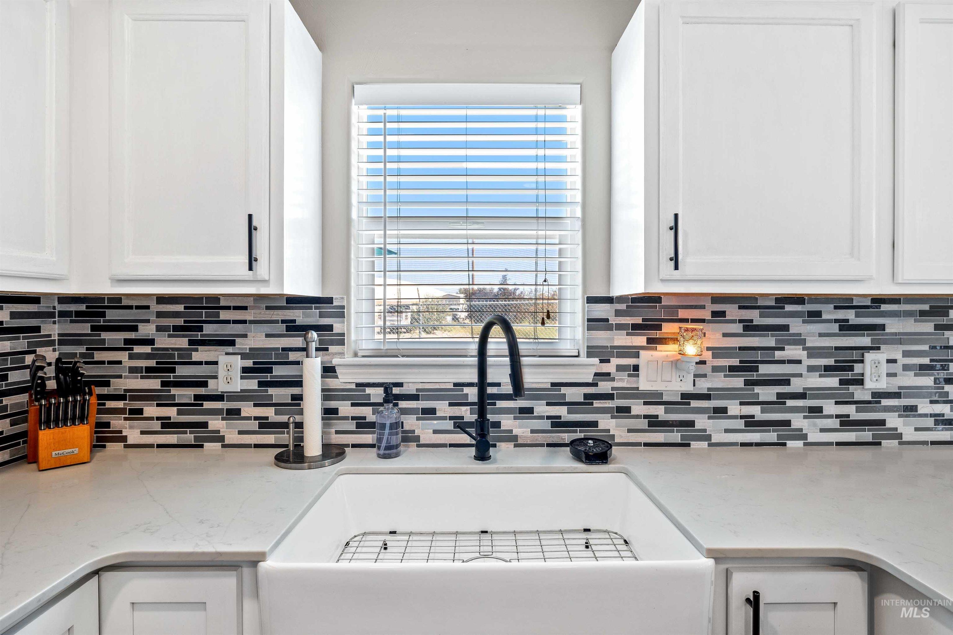 Kitchen featuring light stone countertops, plenty of natural light, white cabinetry, and tasteful backsplash